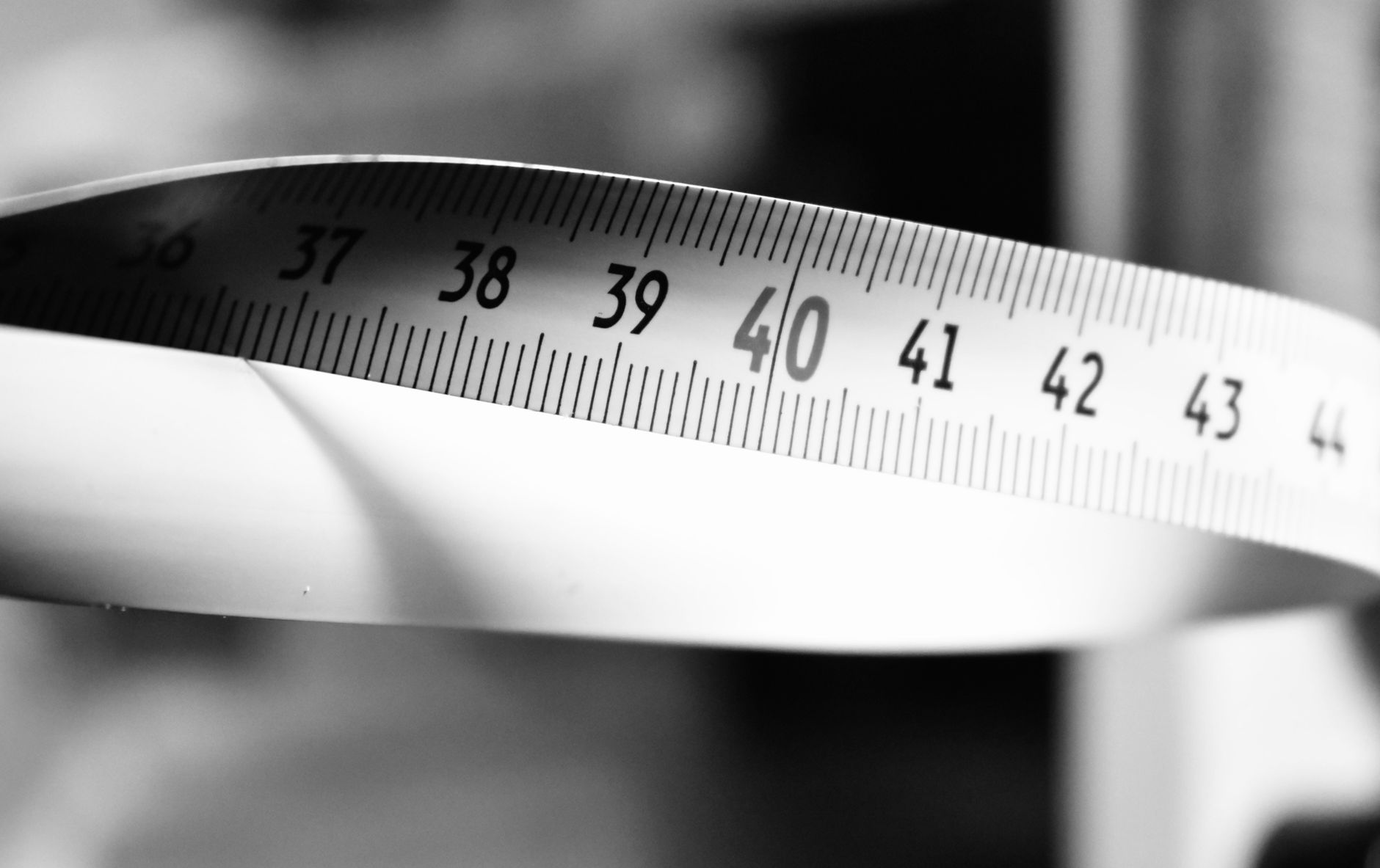 Close‑up of a mother measuring her toddler’s height with a tape measure, soft sunlight through a window