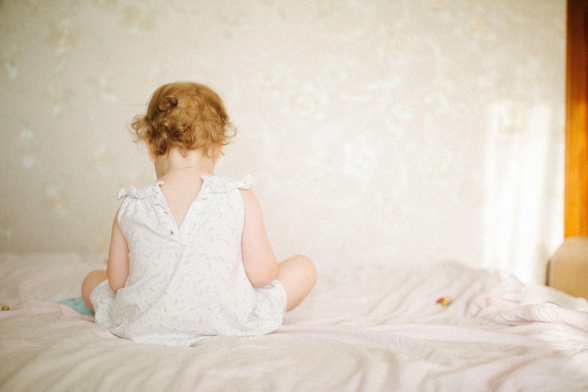 A toddler lying on a blanket, showing facial grimace and leg tension, captured from a side angle with soft natural lighting