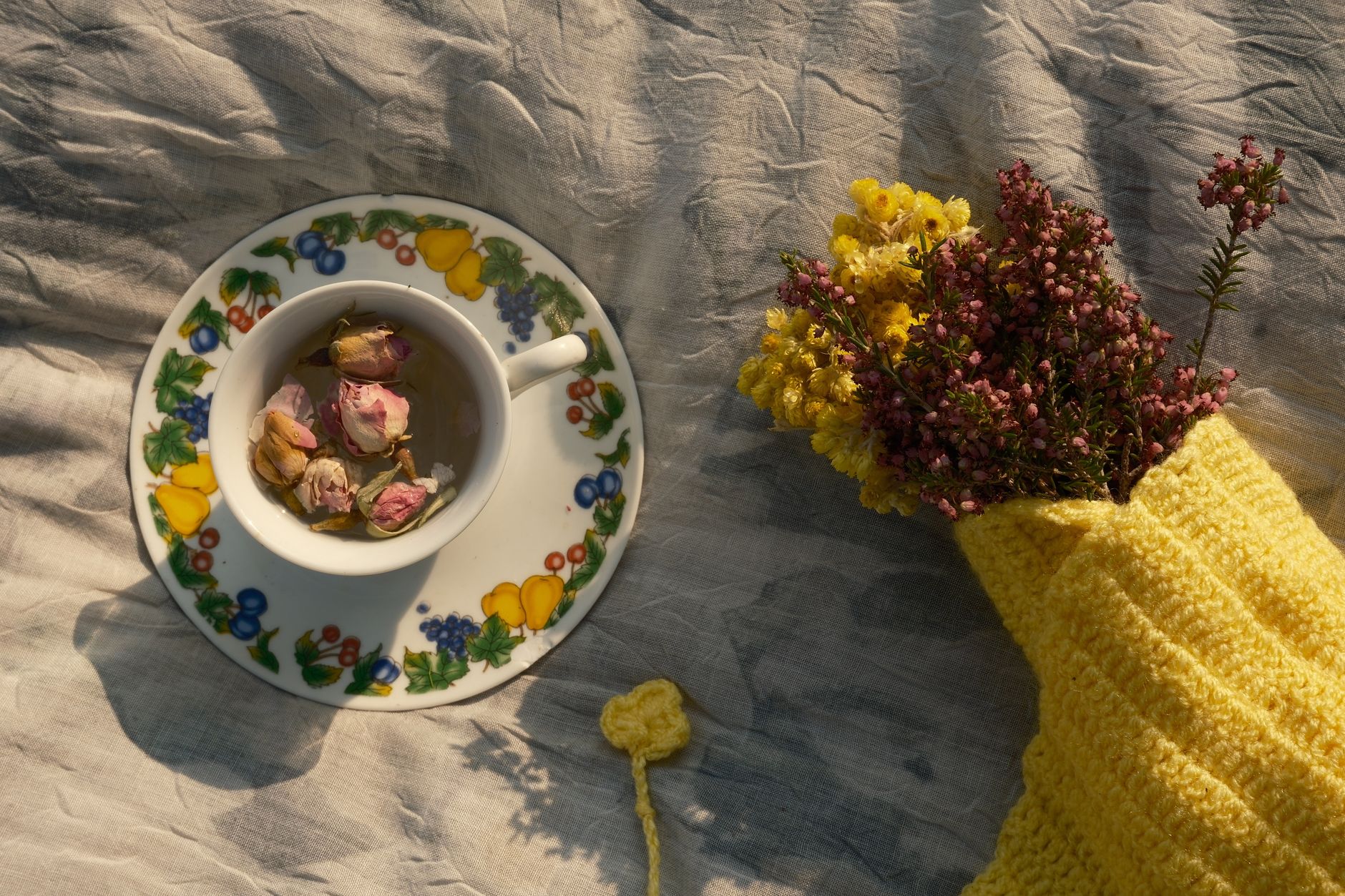 A person's hand reaching for an array of herbal teas and a glass of warm milk on a bedside table, with a soft blanket in the background.