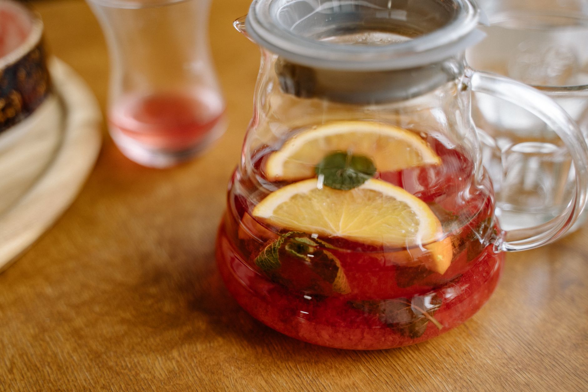 A bright kitchen scene with a pitcher of homemade electrolyte solution, a bowl of fresh fruit, and a pregnant woman's hand reaching for a glass, emphasizing natural hydration options