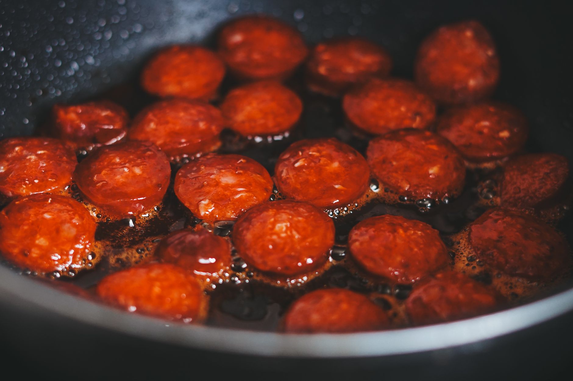 A hand holding a hot skillet with pepperoni slices sizzling, illustrating the proper heating technique for pregnant women