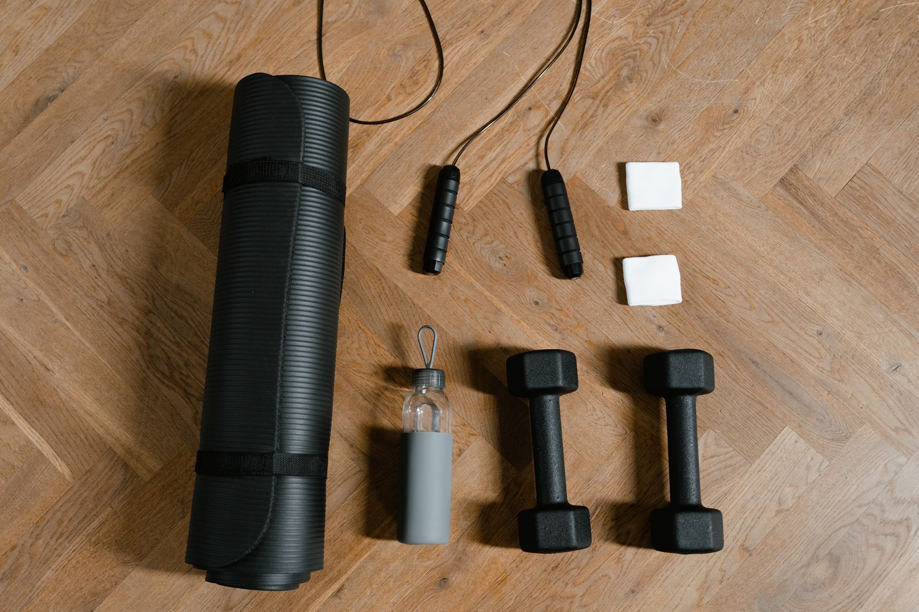 a collection of pregnancy-safe exercise equipment including a yoga mat, water bottle, light dumbbells, and a stationary bike, arranged neatly on a wooden floor