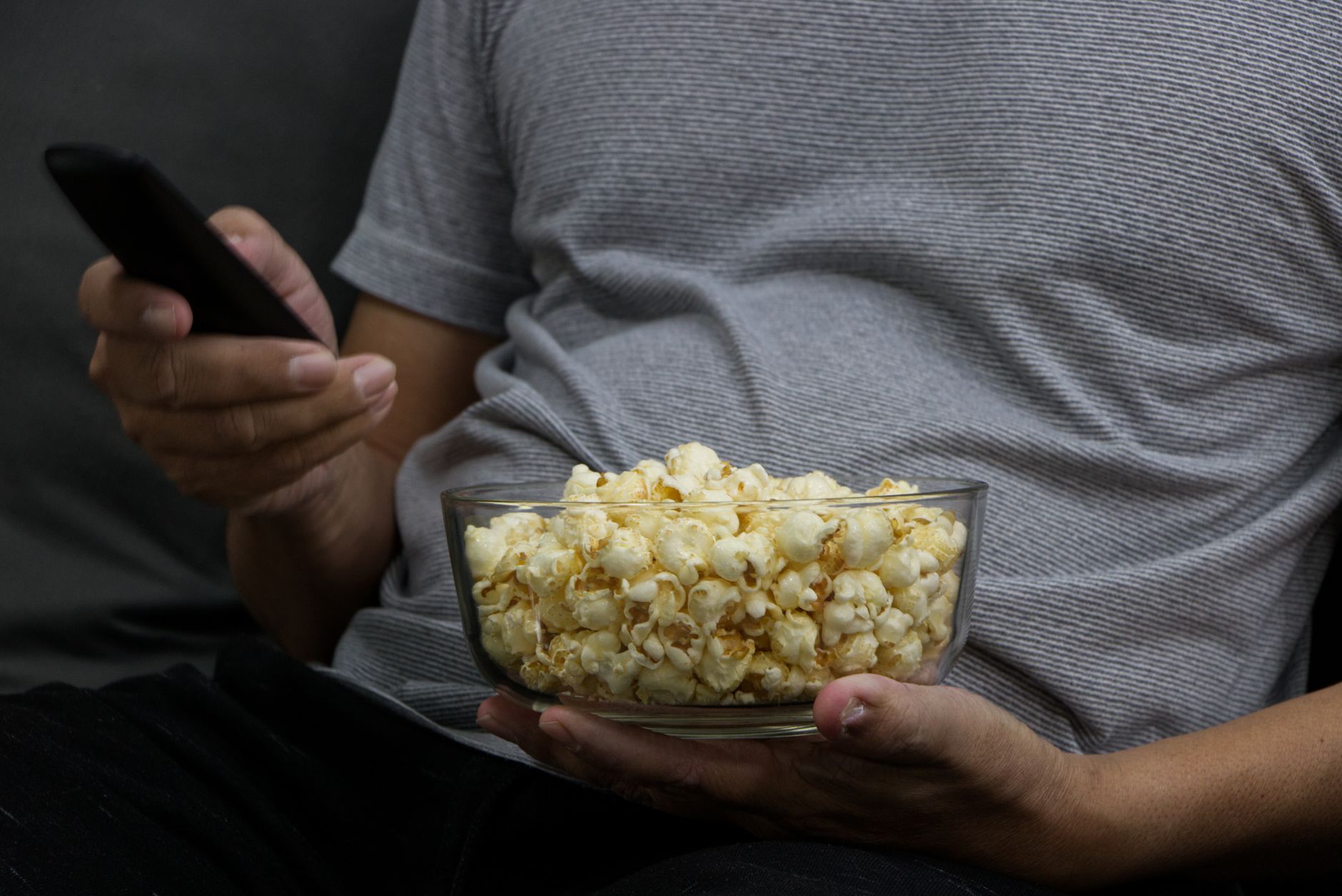 pregnant woman holding a bowl of plain popcorn and smiling while sitting on a couch