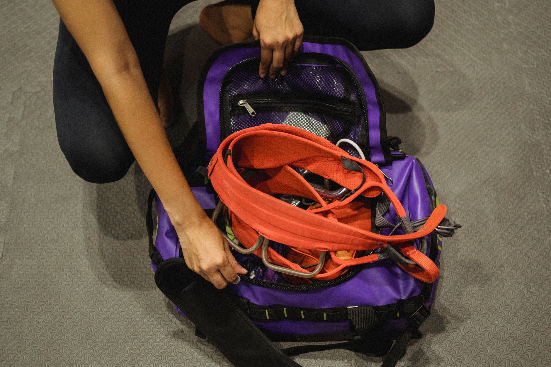 A specialized full-body climbing harness designed for pregnant women, laid out on a clean gym mat, with climbing shoes next to it.