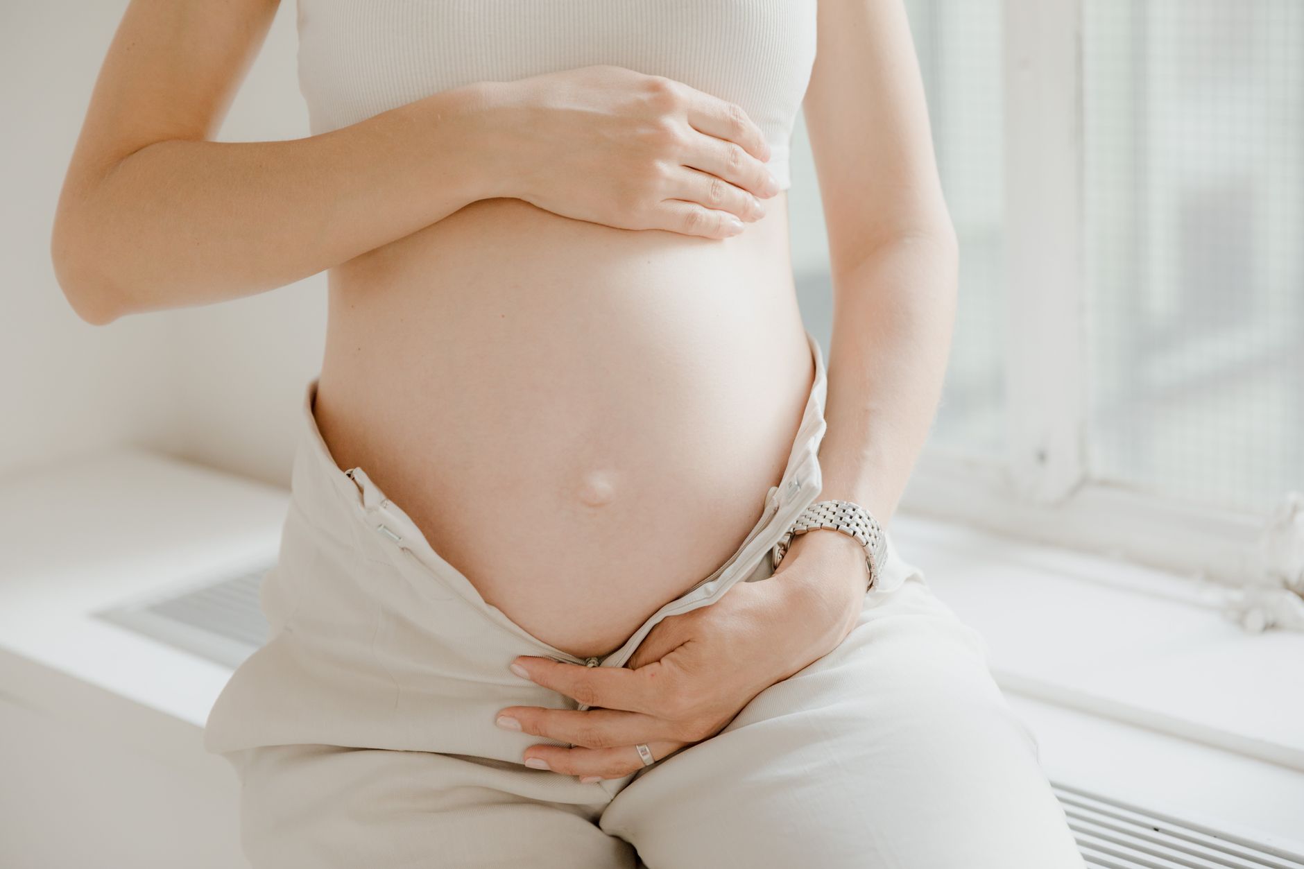 A calm bathroom scene with a hand holding a root touch‑up brush over a pregnant woman's shoulder, soft morning light filtering through a window, emphasizing gentle self‑care