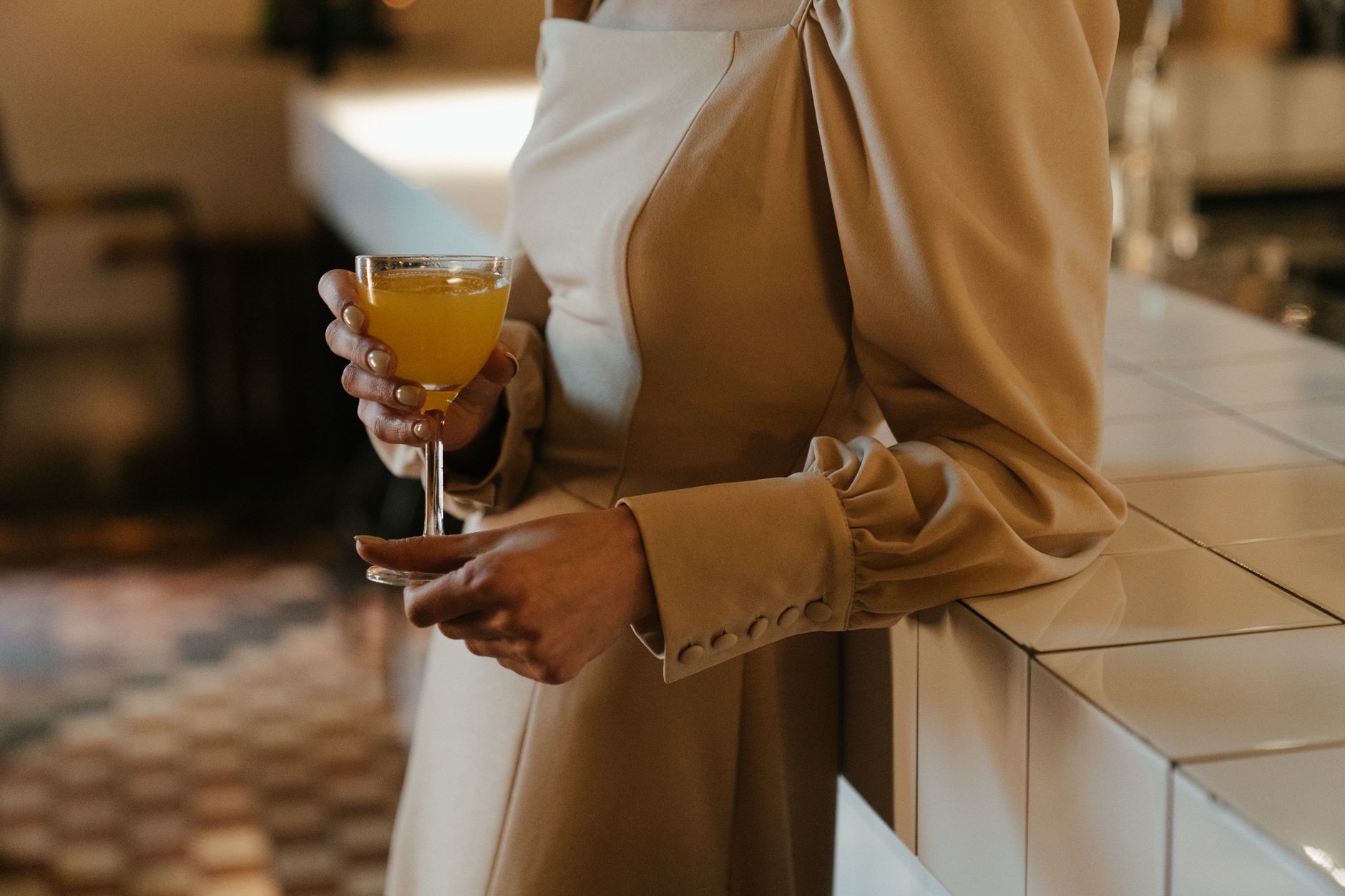 A pregnant woman holding a mocktail in a celebratory setting, with a soft focus on the drink and a subtle hint of a wedding backdrop