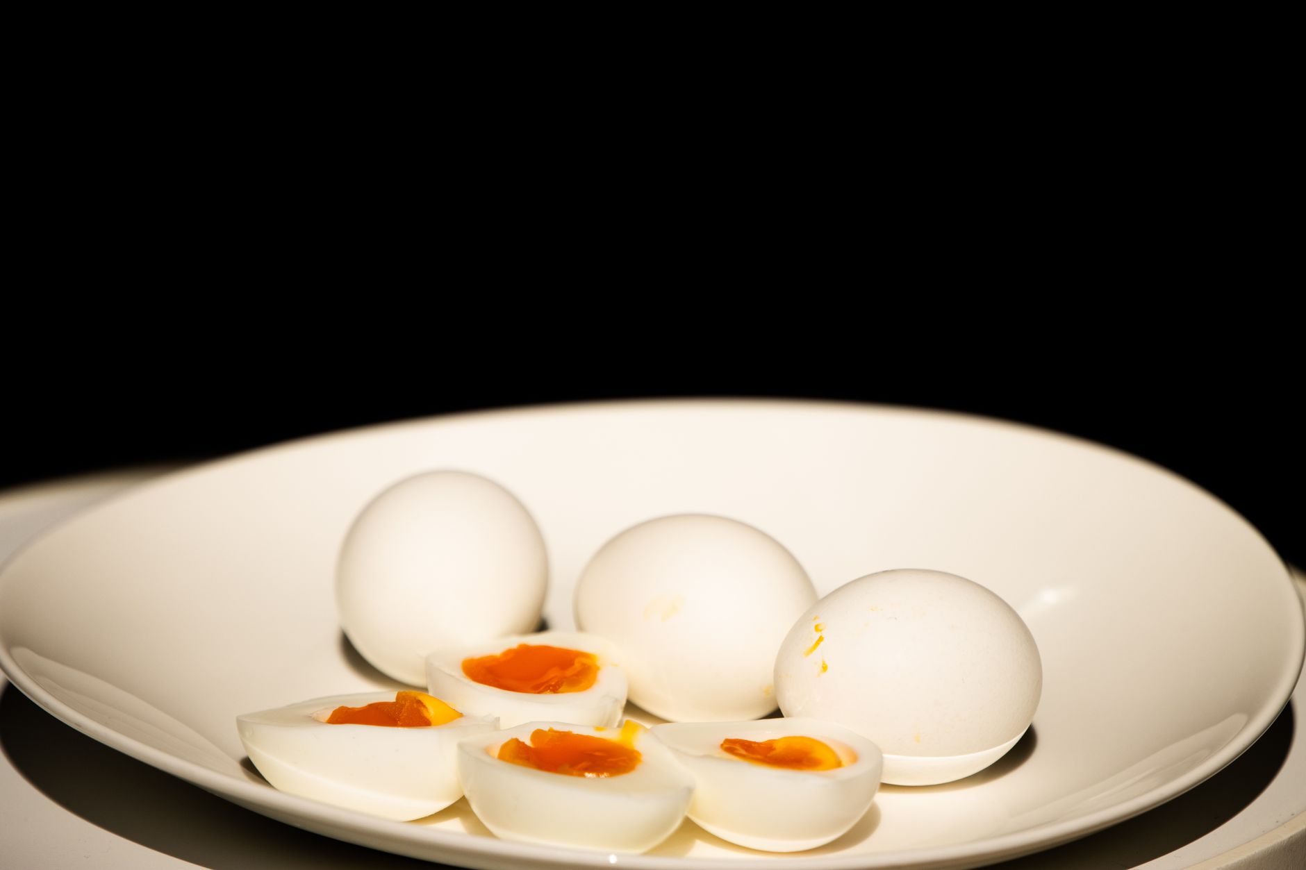 A breakfast plate with a hard‑boiled egg beside a small bowl of sliced salted egg, showing contrast between low‑sodium and high‑sodium options, natural morning light on a clean white plate