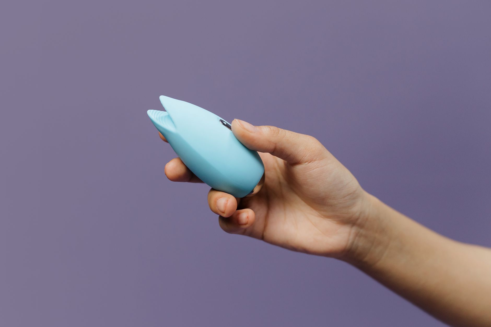 hands holding a small external clitoral stimulator with a soft, flexible design