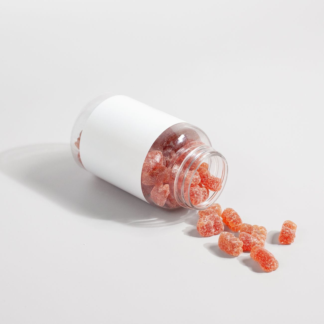 a hand holding a single sour gummy worm next to a prenatal vitamin bottle, soft indoor lighting emphasizing the candy's bright coating