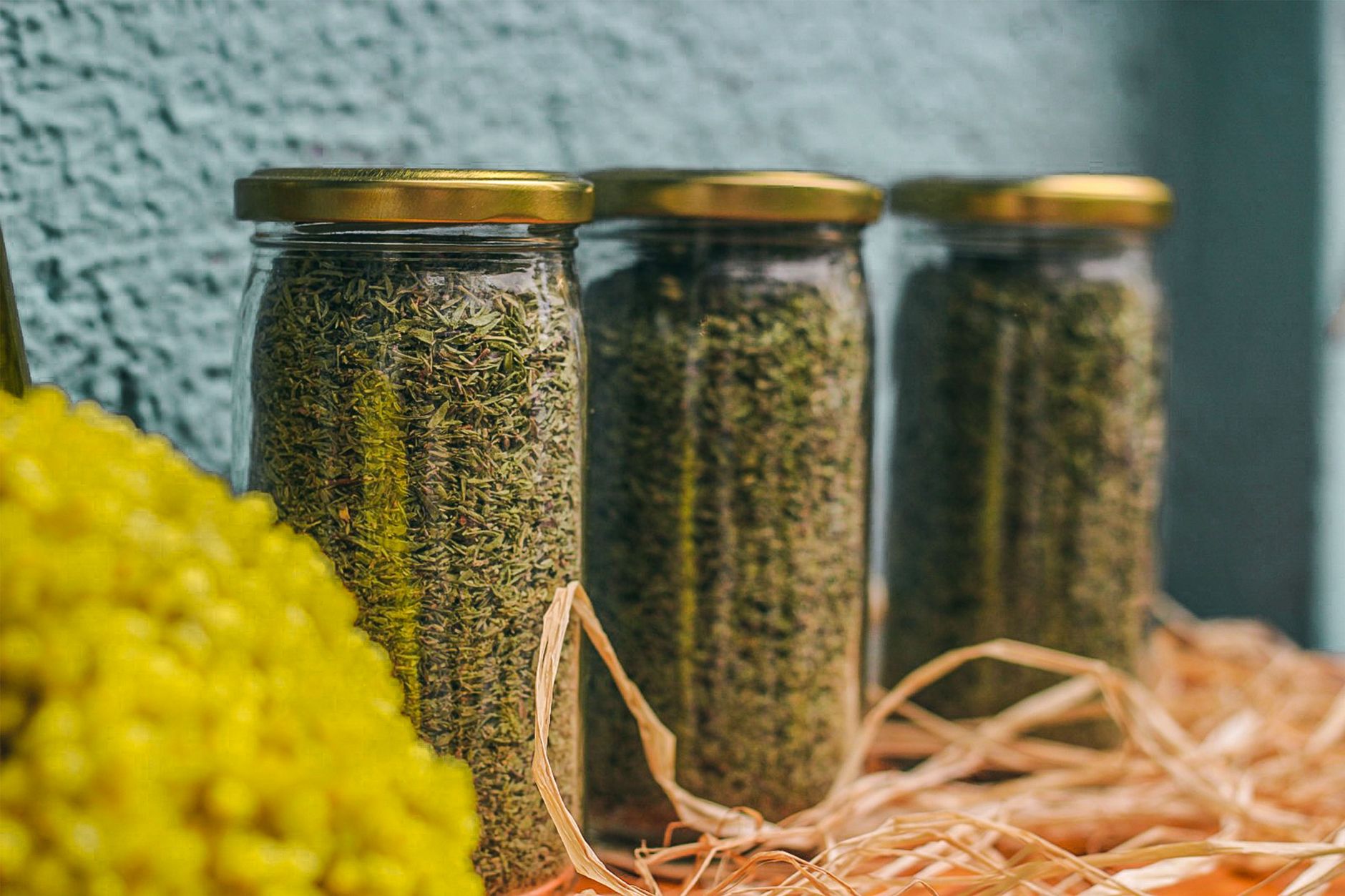Close‑up of a clear glass jar filled with dried spearmint leaves, bright green and ready for brewing, placed on a wooden cutting board