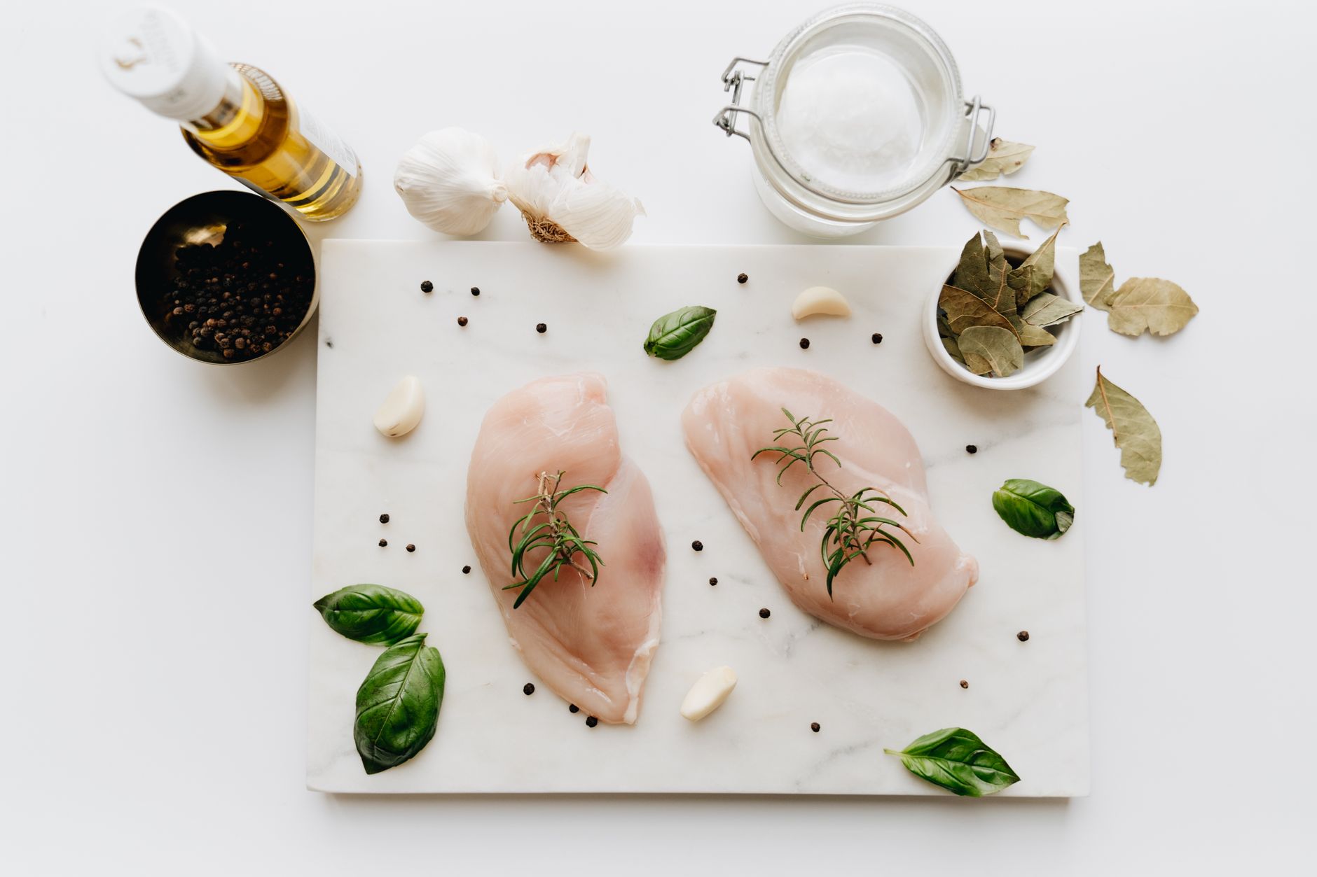 A raw chicken breast on a cutting board next to a meat thermometer, with a pair of disposable gloves and a bottle of bleach solution, representing safe food handling during pregnancy