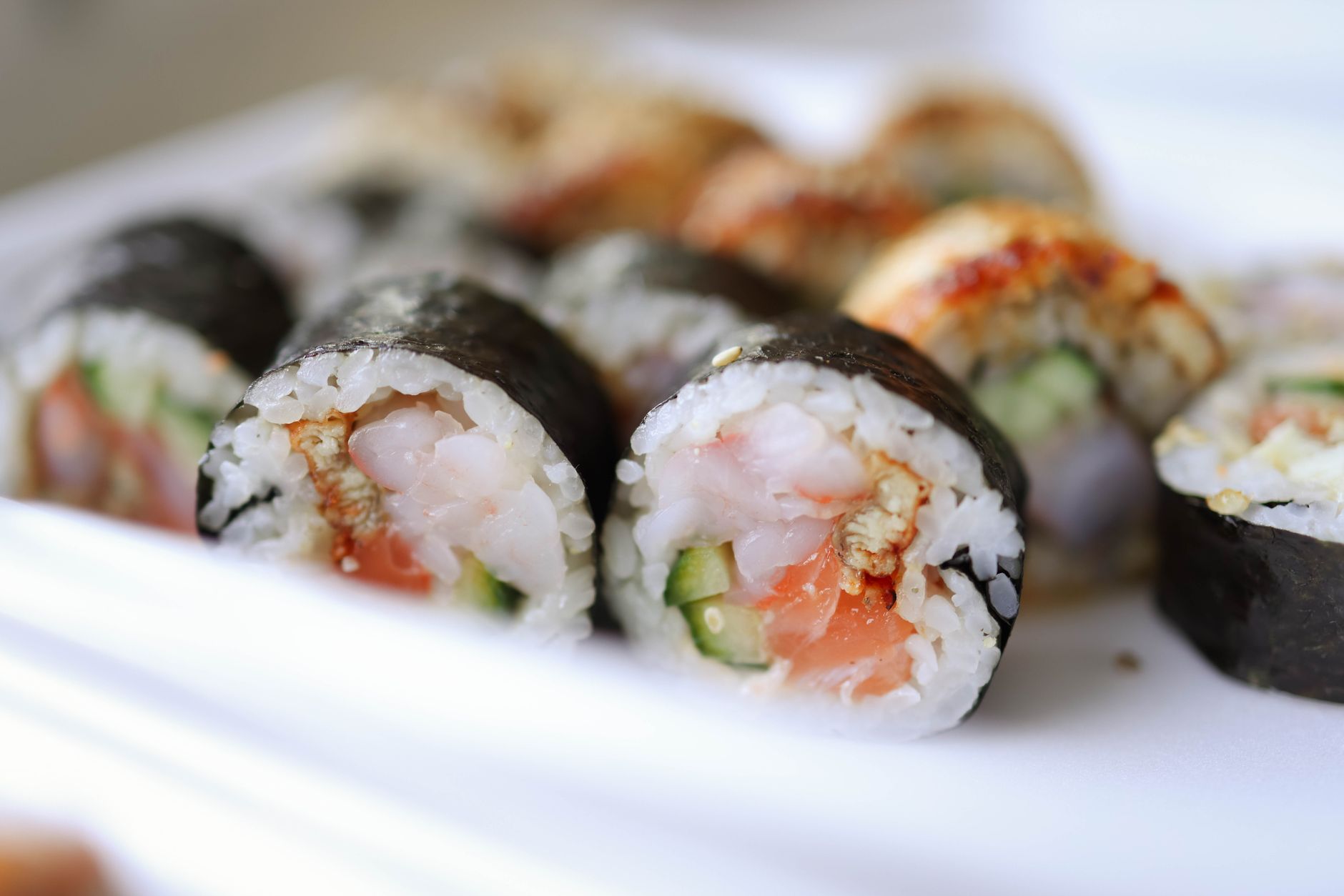 a grocery store sushi aisle featuring pre‑packaged cooked salmon roll, shrimp roll, and avocado roll, with clear labeling for pregnancy safety
