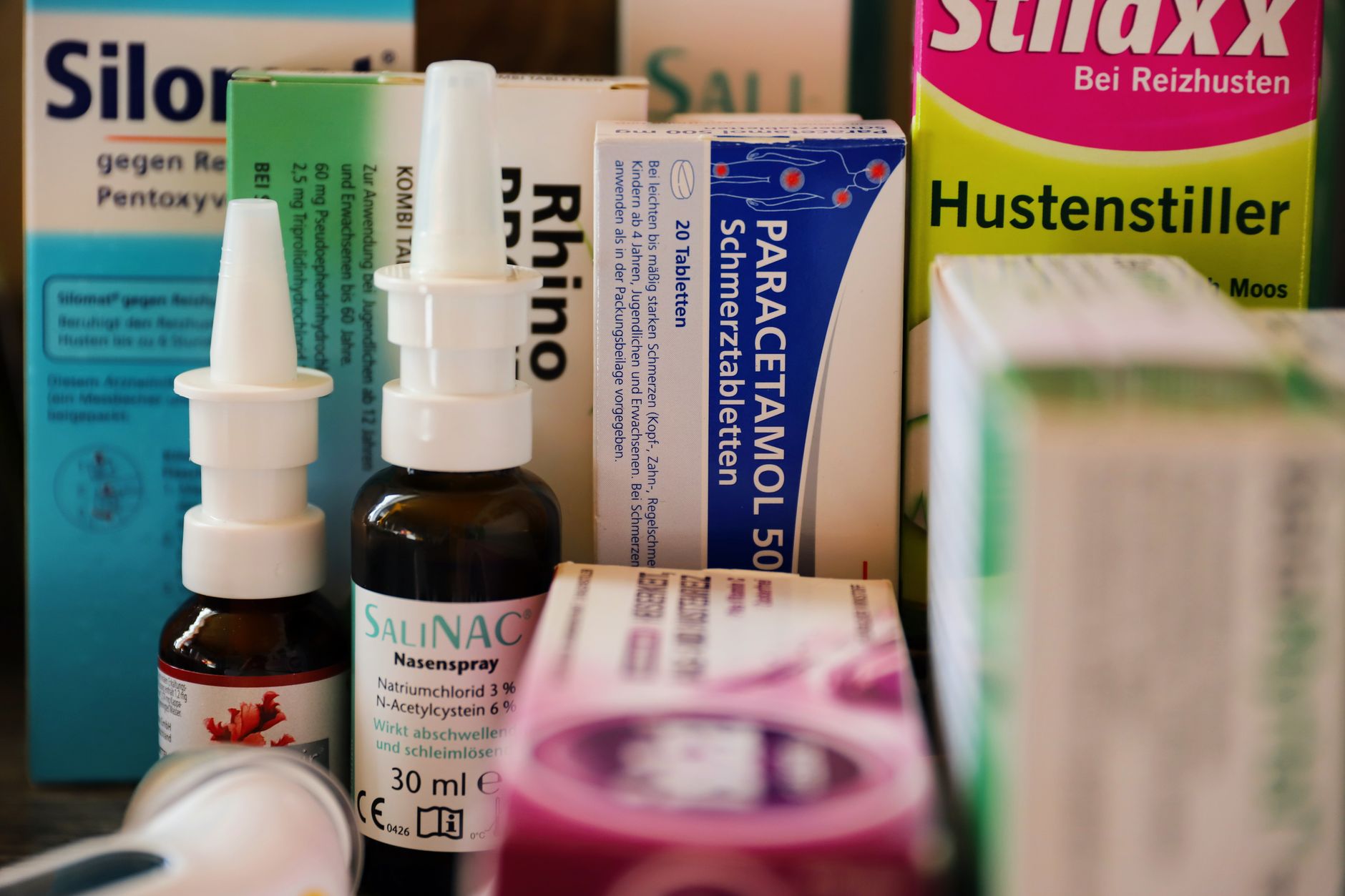 a selection of safe pregnancy cough remedies: a bottle of acetaminophen, a box of guaifenesin, a jar of raw honey, and a saline nasal spray, arranged on a kitchen counter