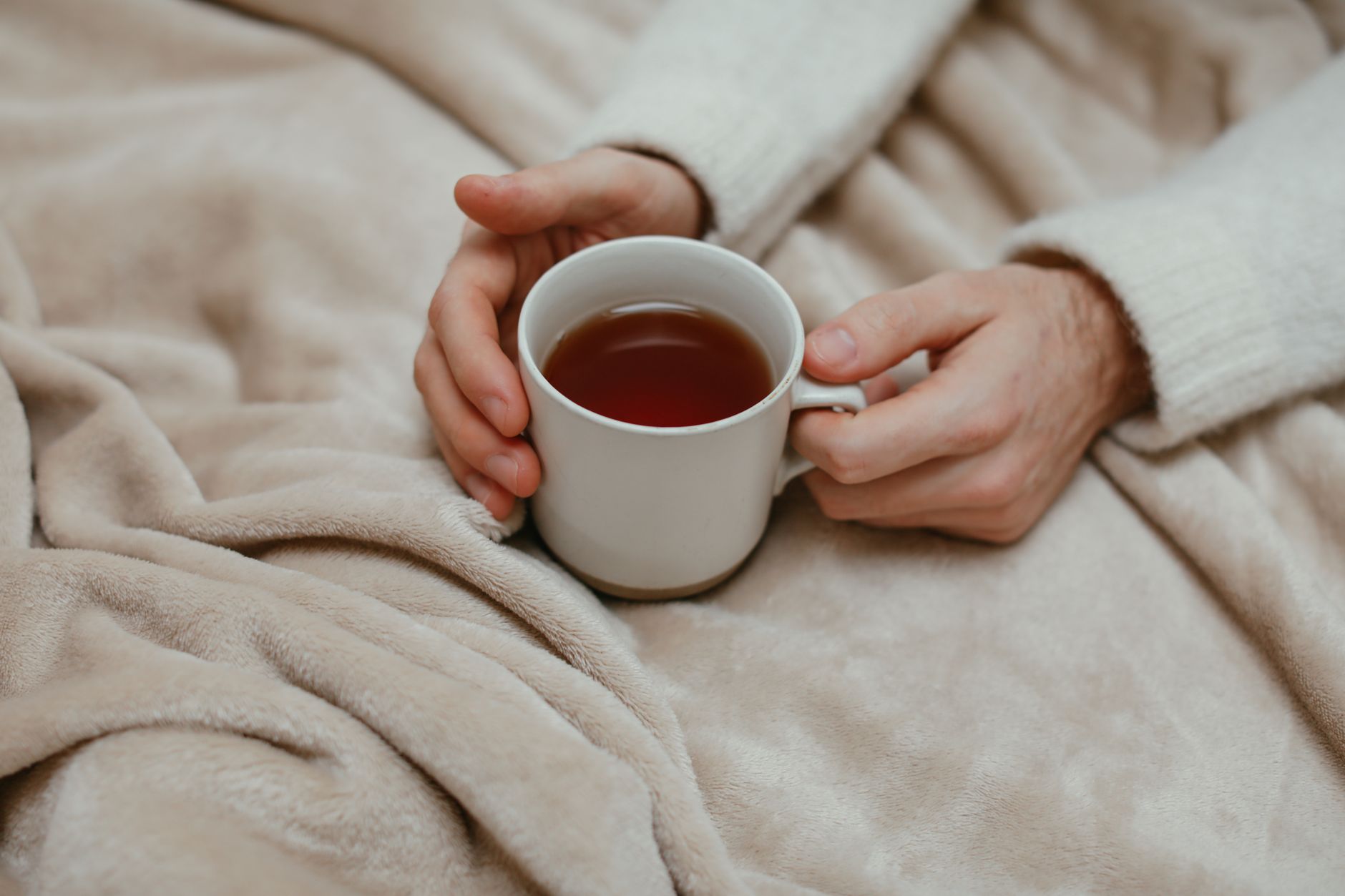 Close‑up of a pregnant woman's hands holding a warm mug of tea, a soft blanket draped over a sofa, morning sunlight through a window