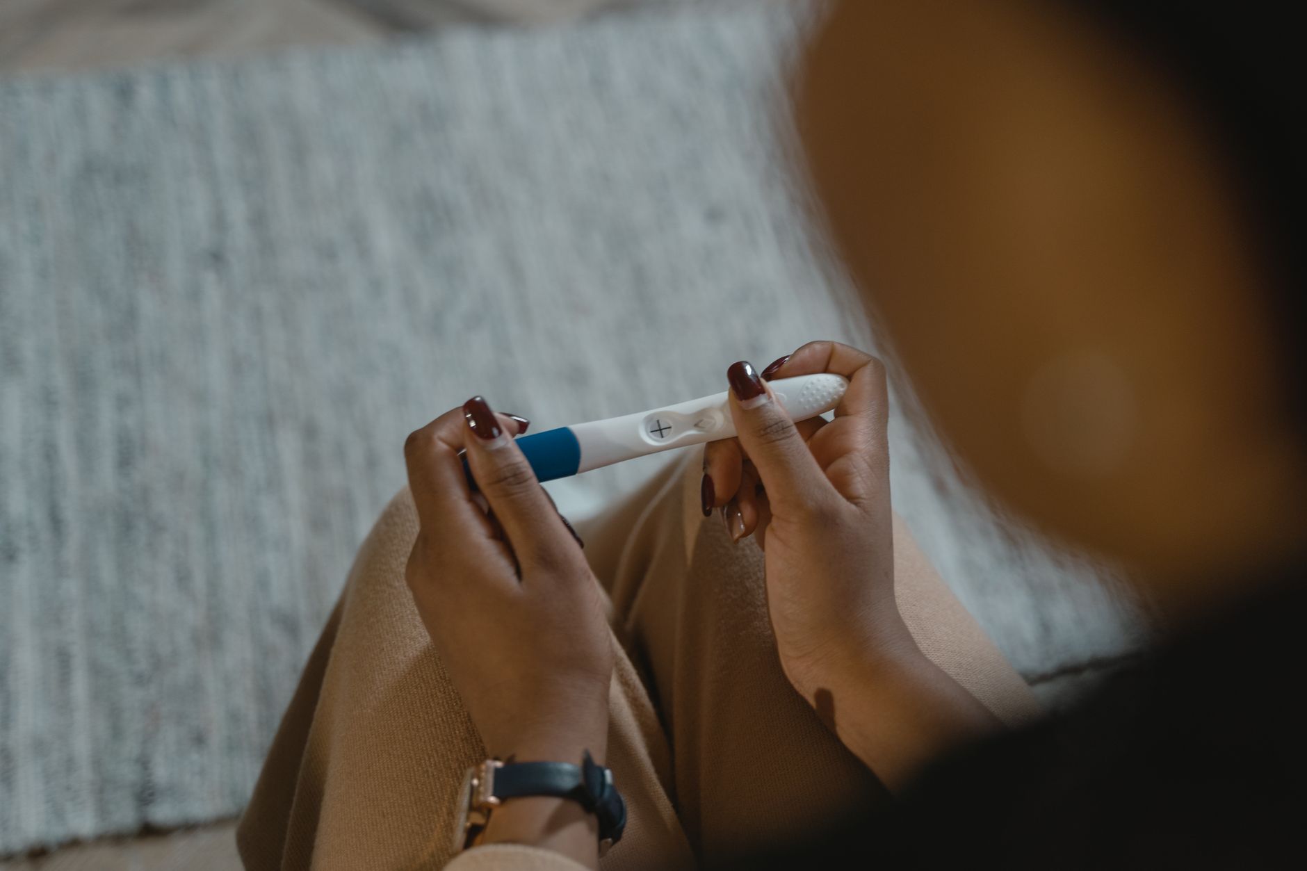 A pair of hands holding a pregnancy test and a swab test for STIs, placed side by side on a white countertop with a plant in the background