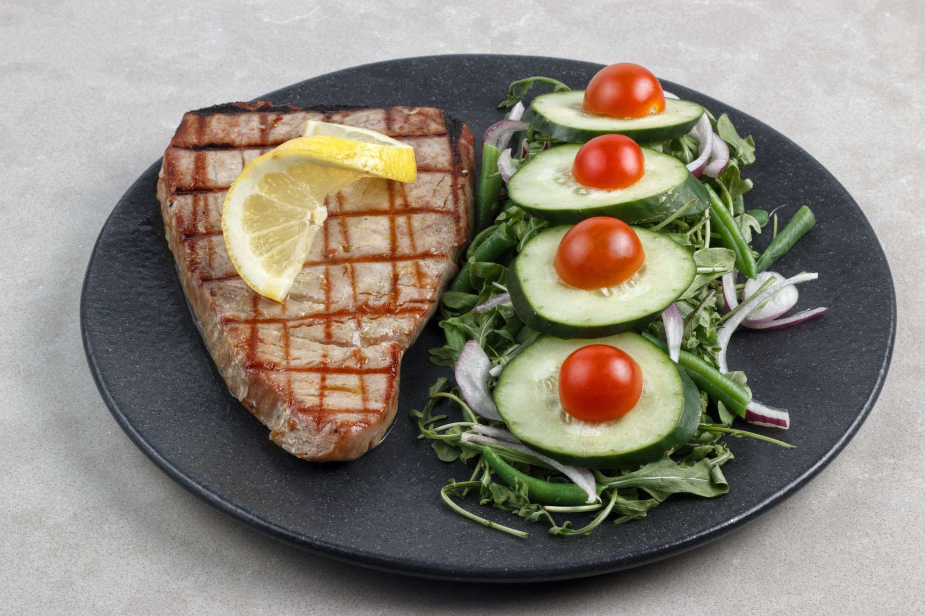 A pregnant woman holding a cooked tuna steak on a plate beside a lemon wedge, illustrating safe cooking methods for tuna during pregnancy