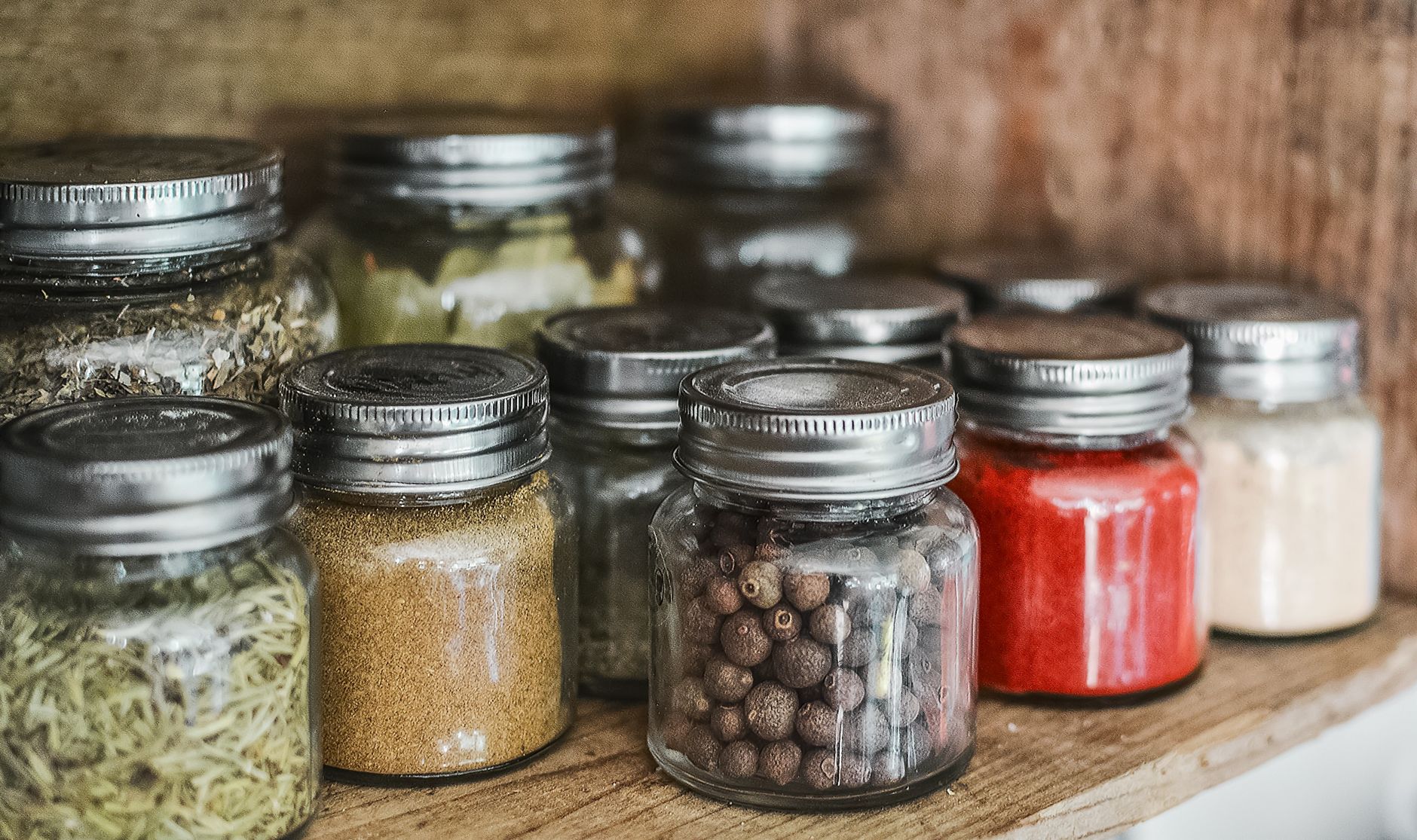 a tidy kitchen shelf displaying a row of spice jars, a labeled turmeric jar, a black pepper grinder, and a small glass bottle of honey, soft daylight streaming through a window