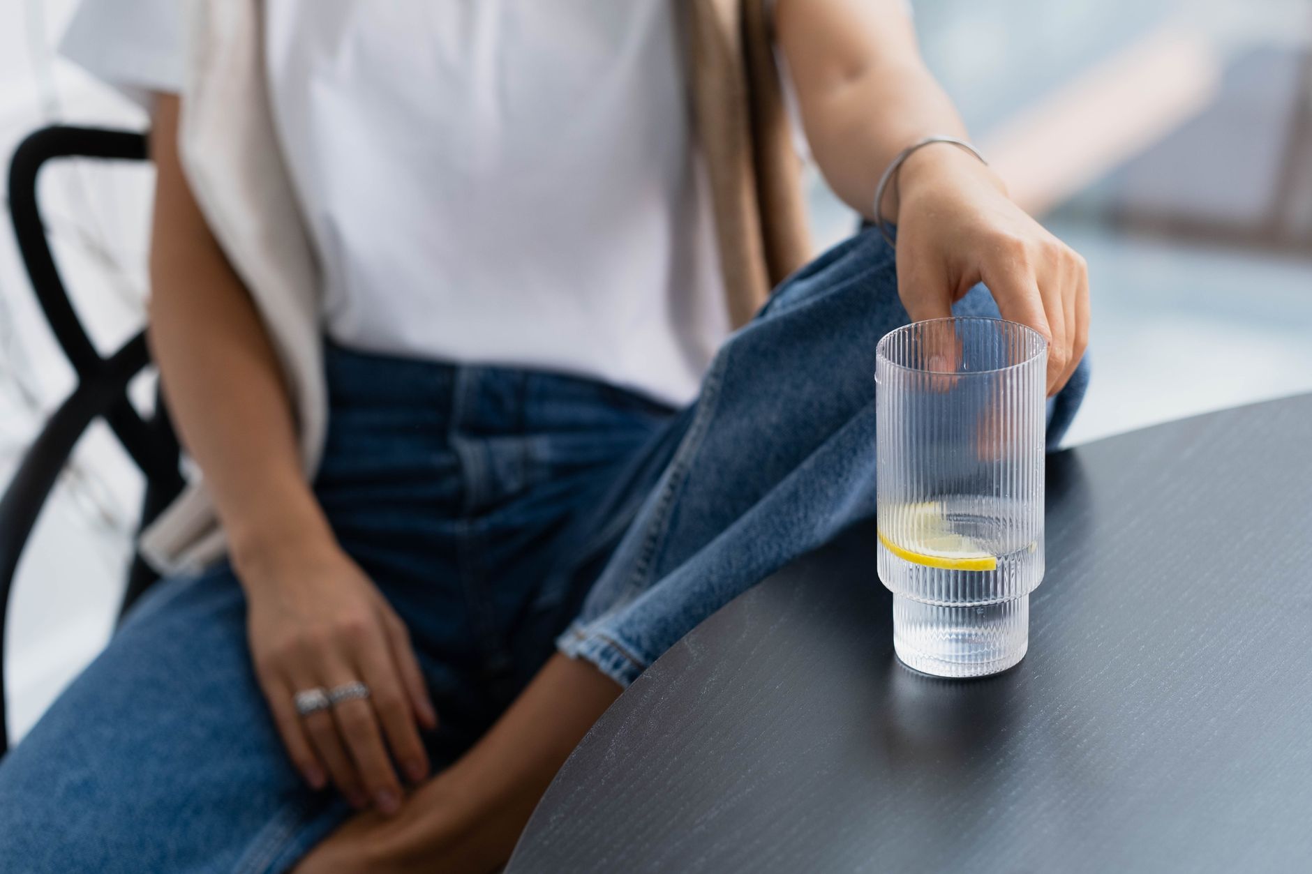 A pregnant person's hand gently resting on their baby bump, with a glass of sparkling water and lemon on a nearby table, soft lighting, no face visible