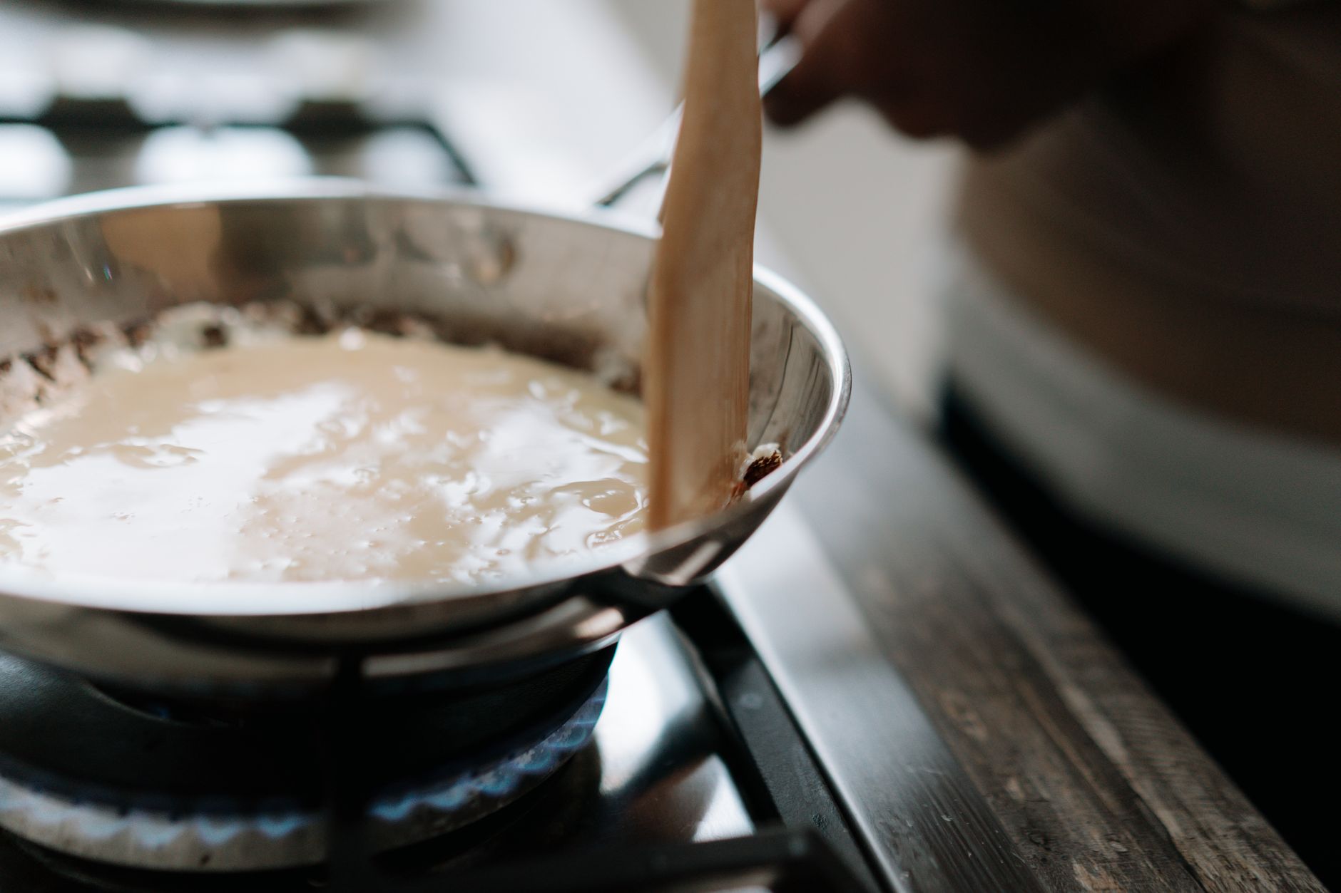 close‑up of a whisk stirring a glossy, pale yellow zabaglione mixture in a stainless‑steel saucepan, steam rising, soft kitchen lighting