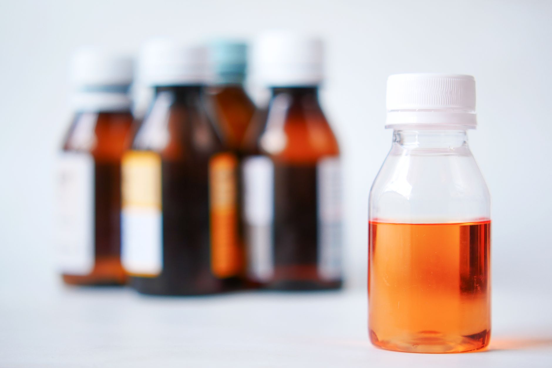Close-up of a pediatrician’s office shelf with labeled cough syrups, including a bottle of Zarbee's honey cough syrup alongside a child-safe dosing cup and a humidifier