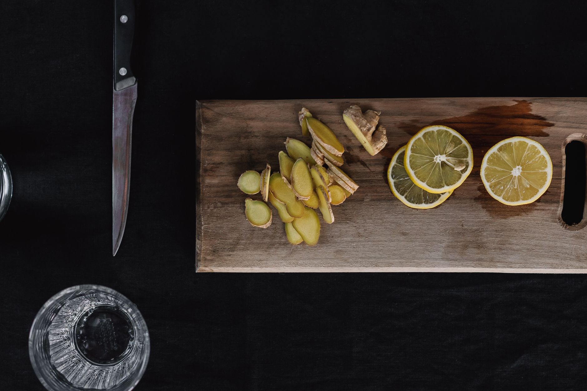 Fresh ginger root sliced on a wooden cutting board beside a glass of water, illustrating a natural alternative for nausea relief during pregnancy