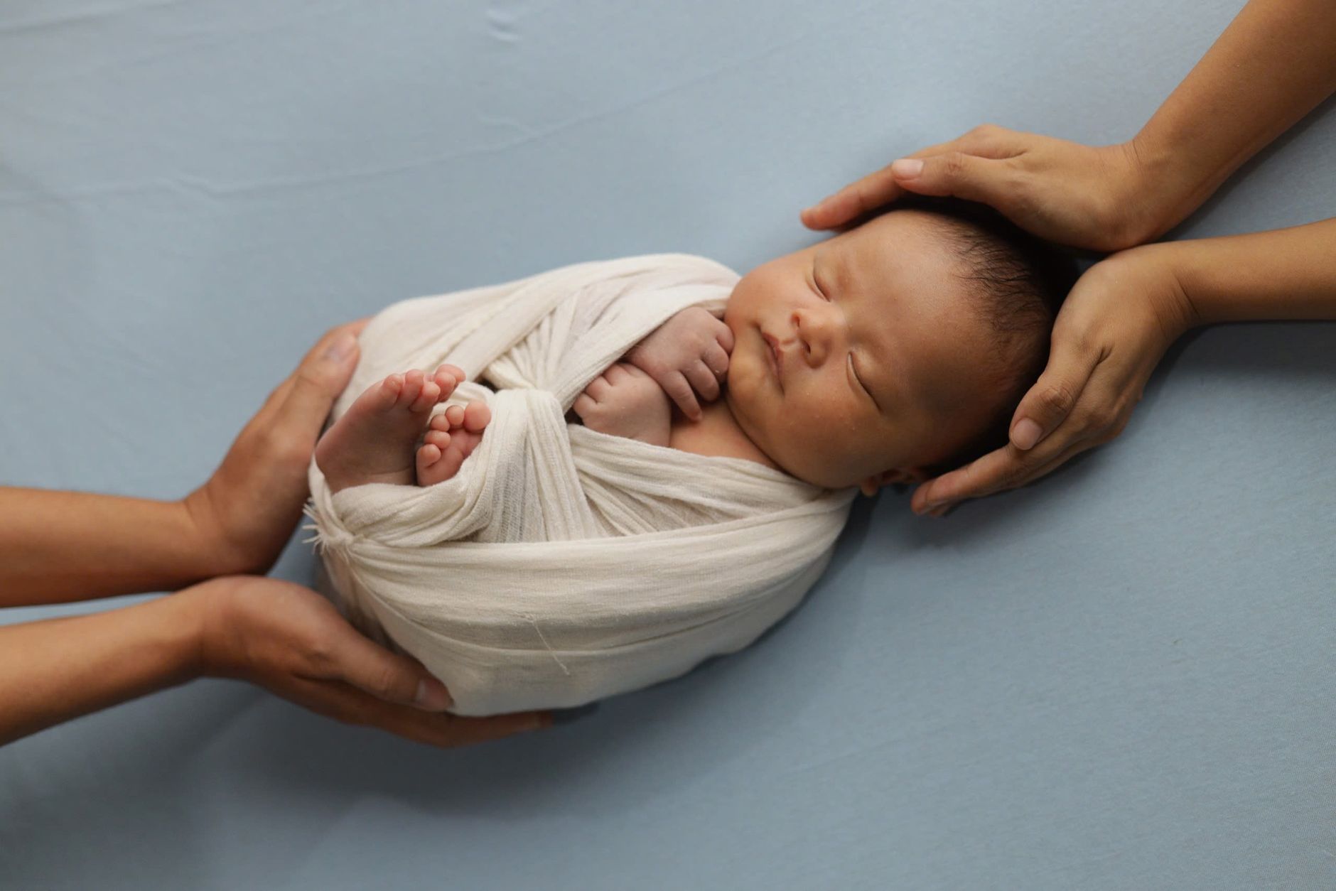 A parent's hands gently supporting a newborn baby lying on a fiber optic phototherapy blanket at home, soft light, cozy setting