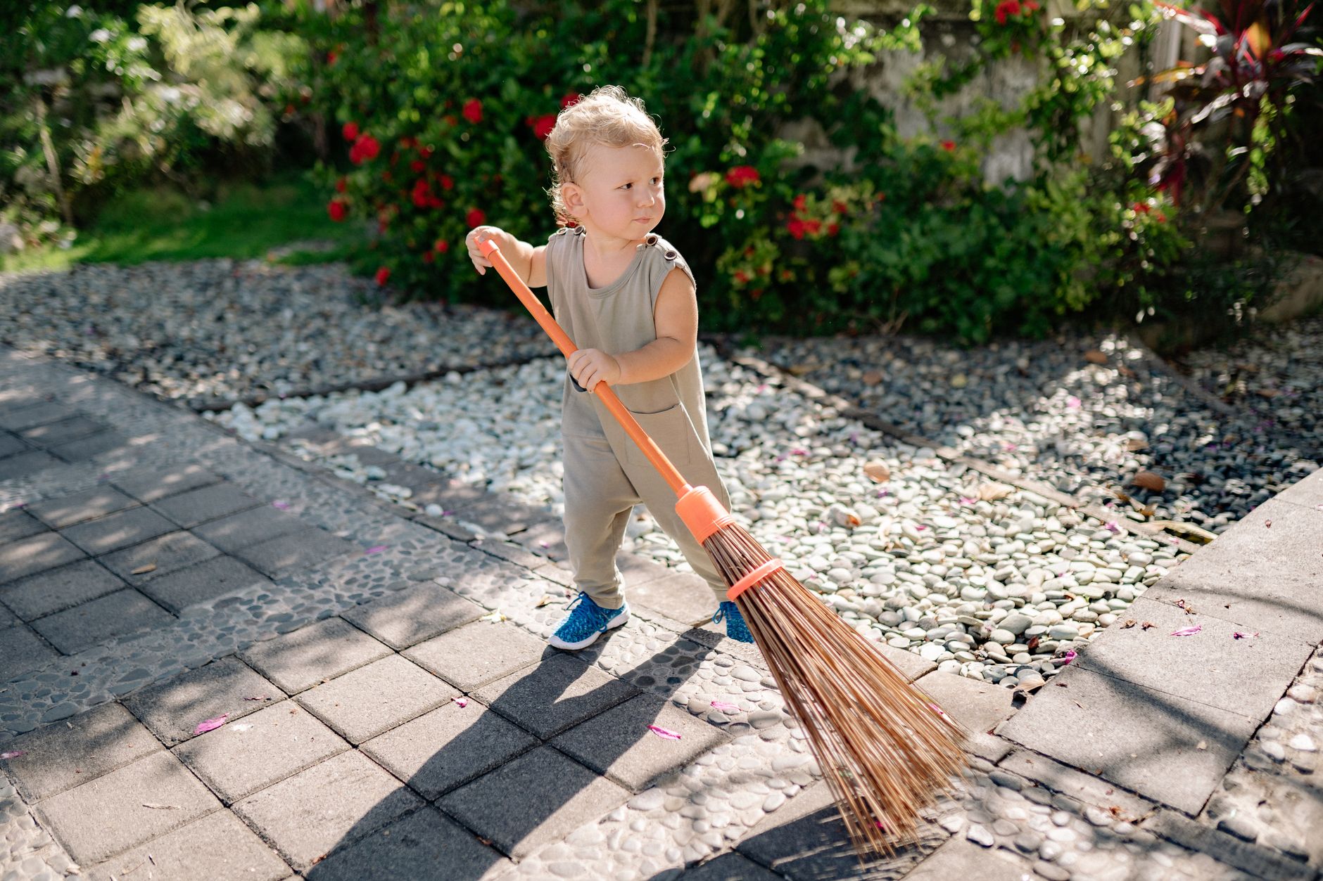 A toddler in a pink dress holding a toy broom, sweeping the floor