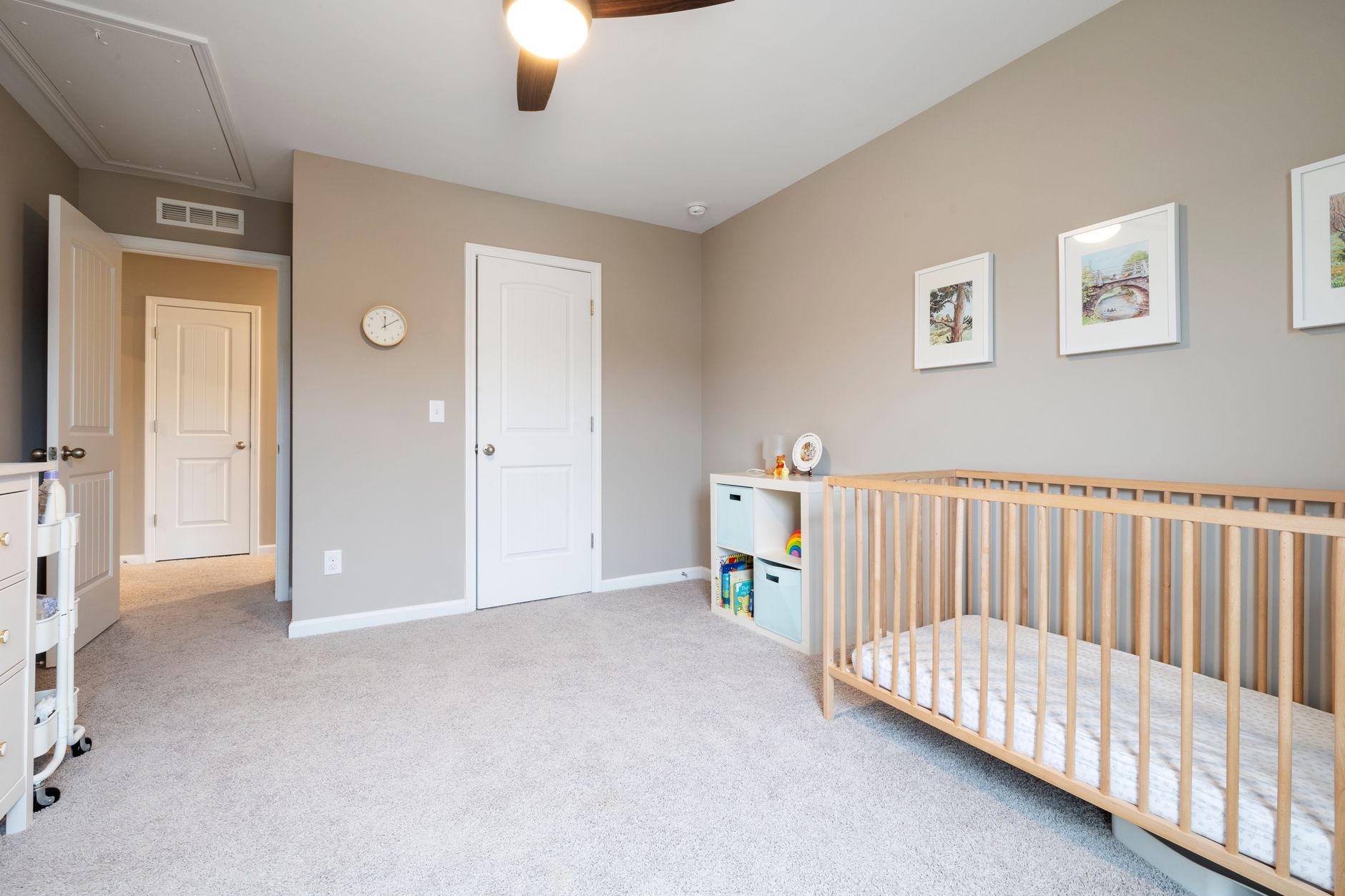 A minimalist nursery with a clear bin of diapers, a wall-mounted shelf for books, and a crib with soft blankets