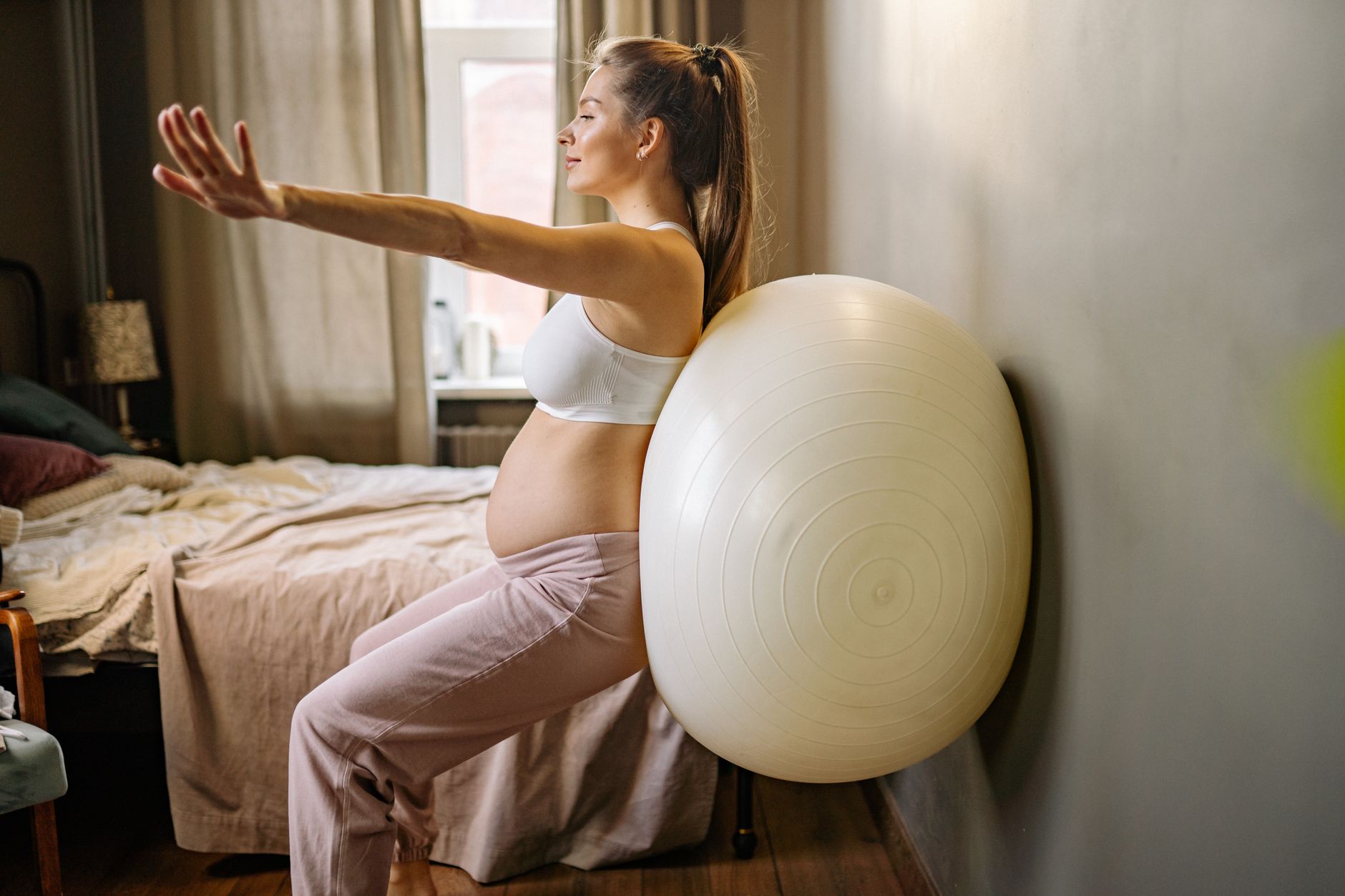 Pregnant woman gently rocking on a birthing ball in a bright, airy room with soft natural light