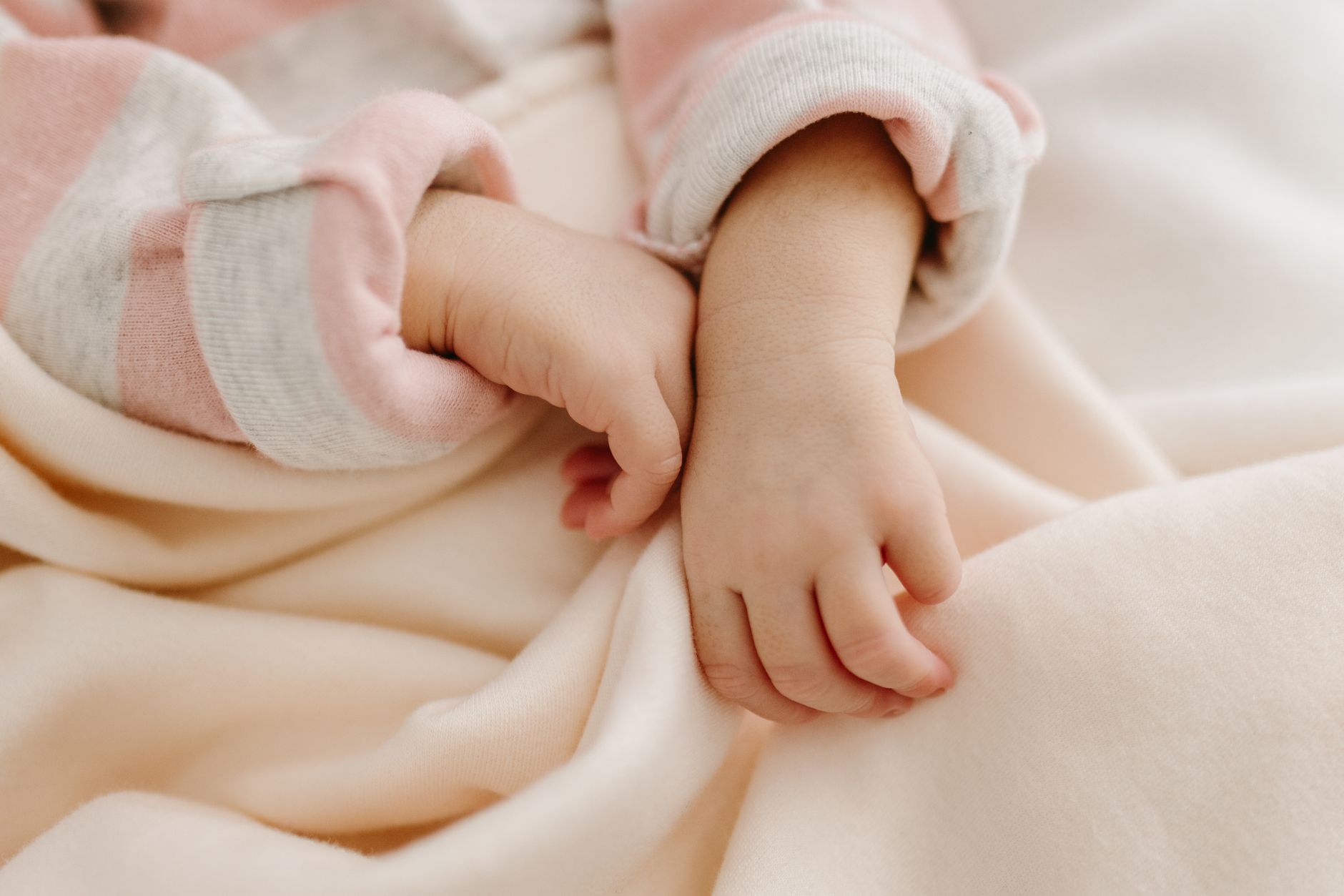 Close‑up of a newborn’s tiny hand holding a soft baby blanket, warm natural light, gentle focus, highlighting the delicate skin