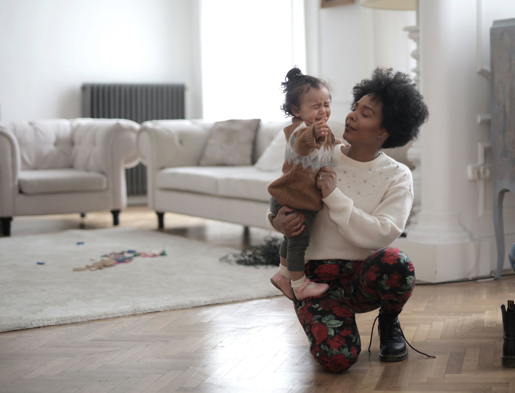 A smiling mother holding her newborn baby, while her toddler plays happily on the floor beside them, depicting a calm family scene.