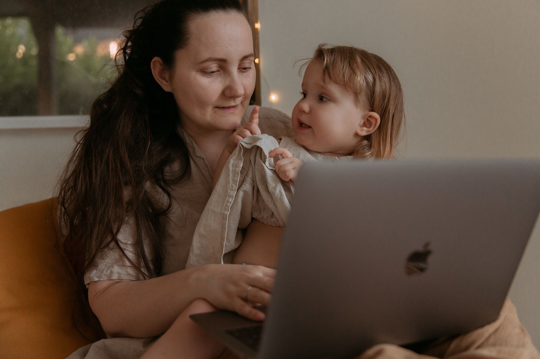 A mom and toddler sitting together on a bed, listening to a meditation app with headphones.