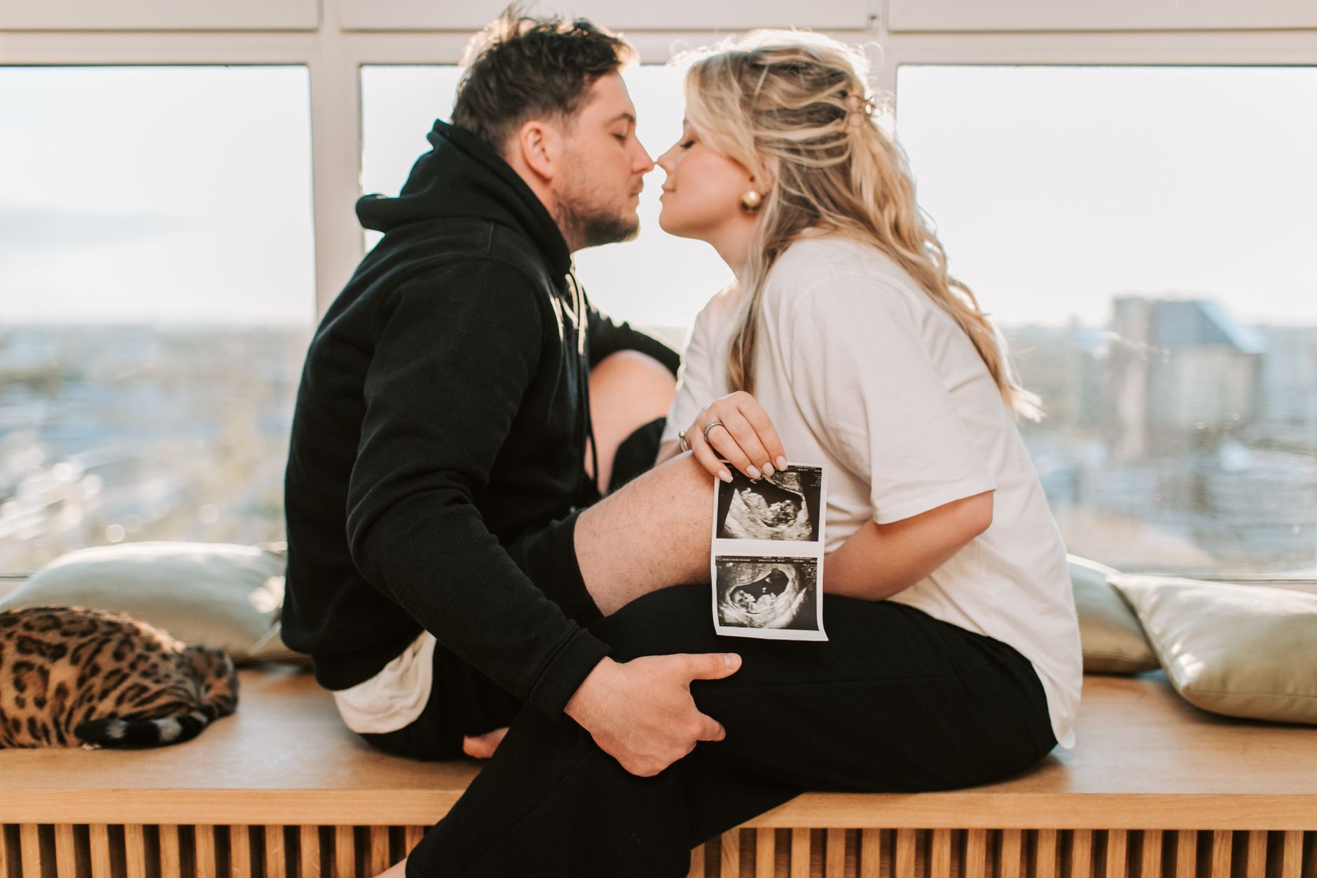 Pregnant woman sitting at a kitchen table, holding a printed ultrasound report, looking relieved as she discusses results with her partner