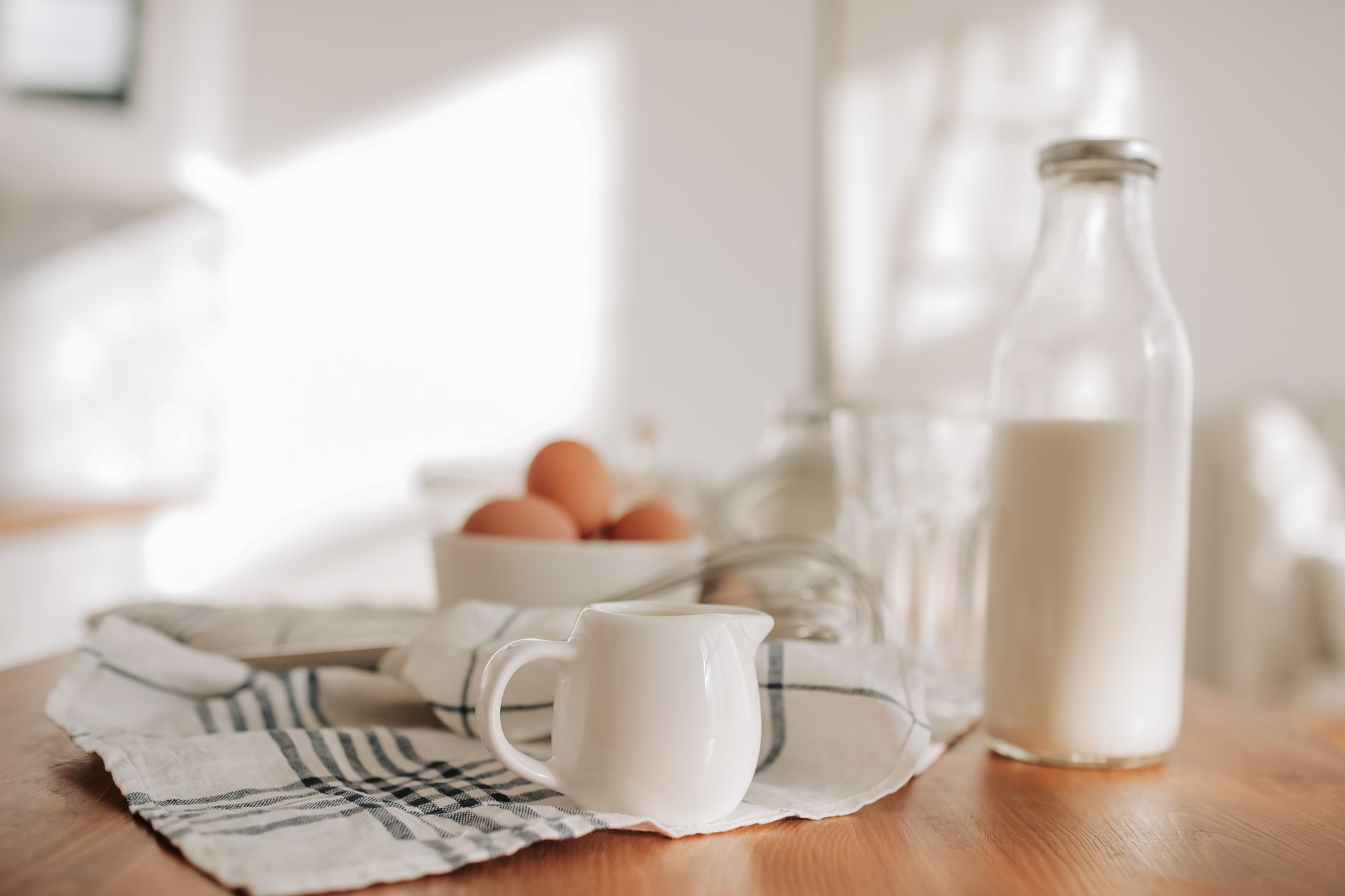 Close‑up of a glass of milk beside a small bowl of golden colostrum, set on a wooden table with fresh herbs