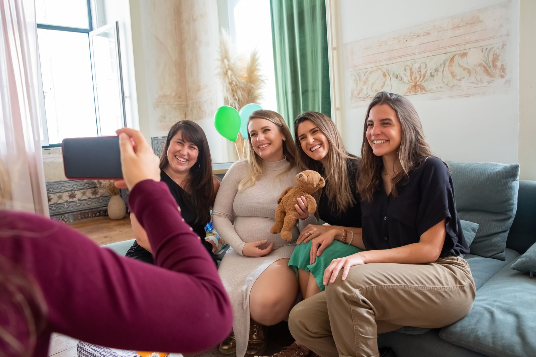 A group of friends sitting in a circle in a living room, one person holding a framed photo of a baby, with soft lighting and a cozy atmosphere.