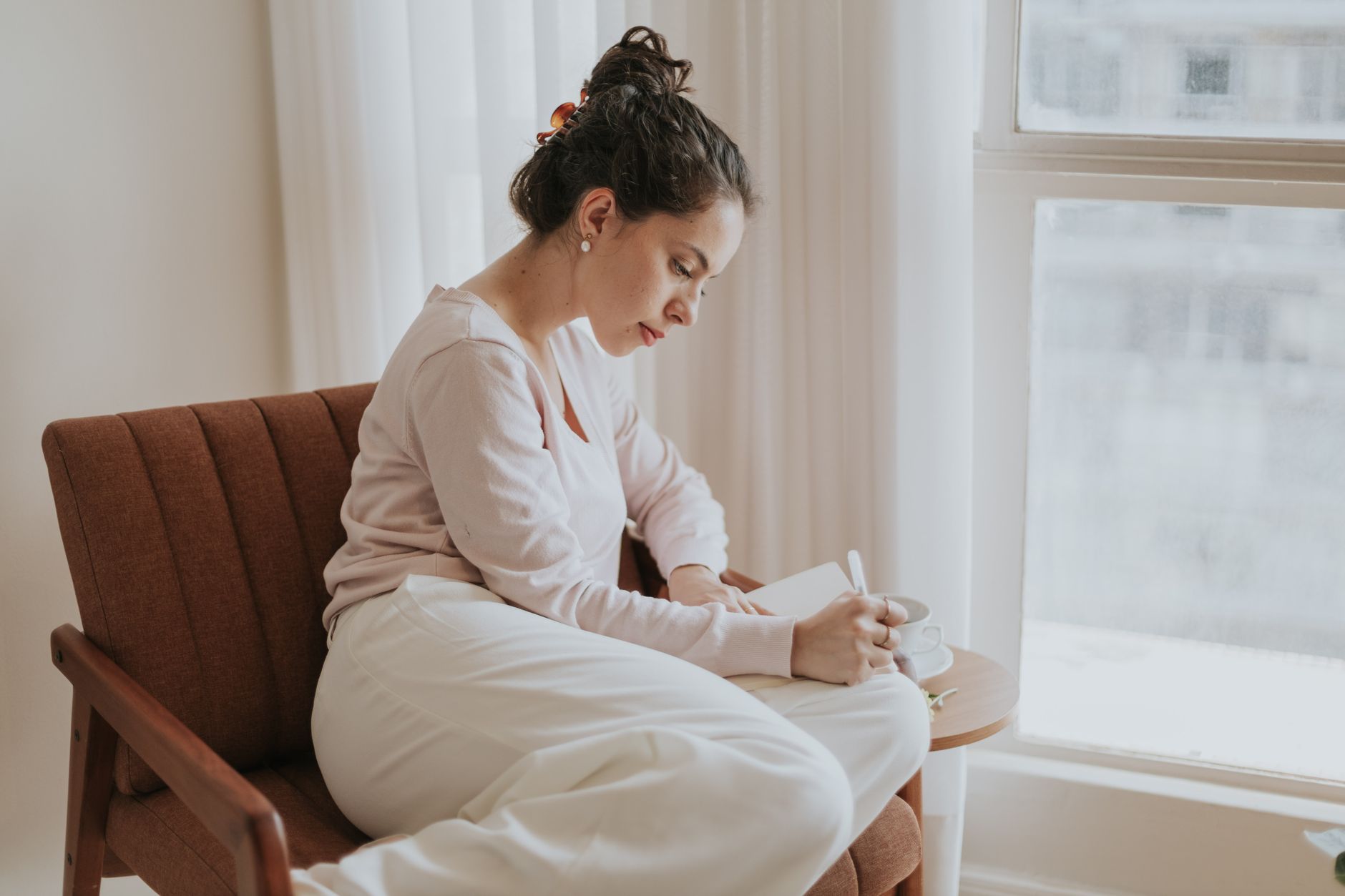 A woman writing in a journal with a cup of tea, in a calm and inviting setting. The focus is on the act of journaling and self-reflection.