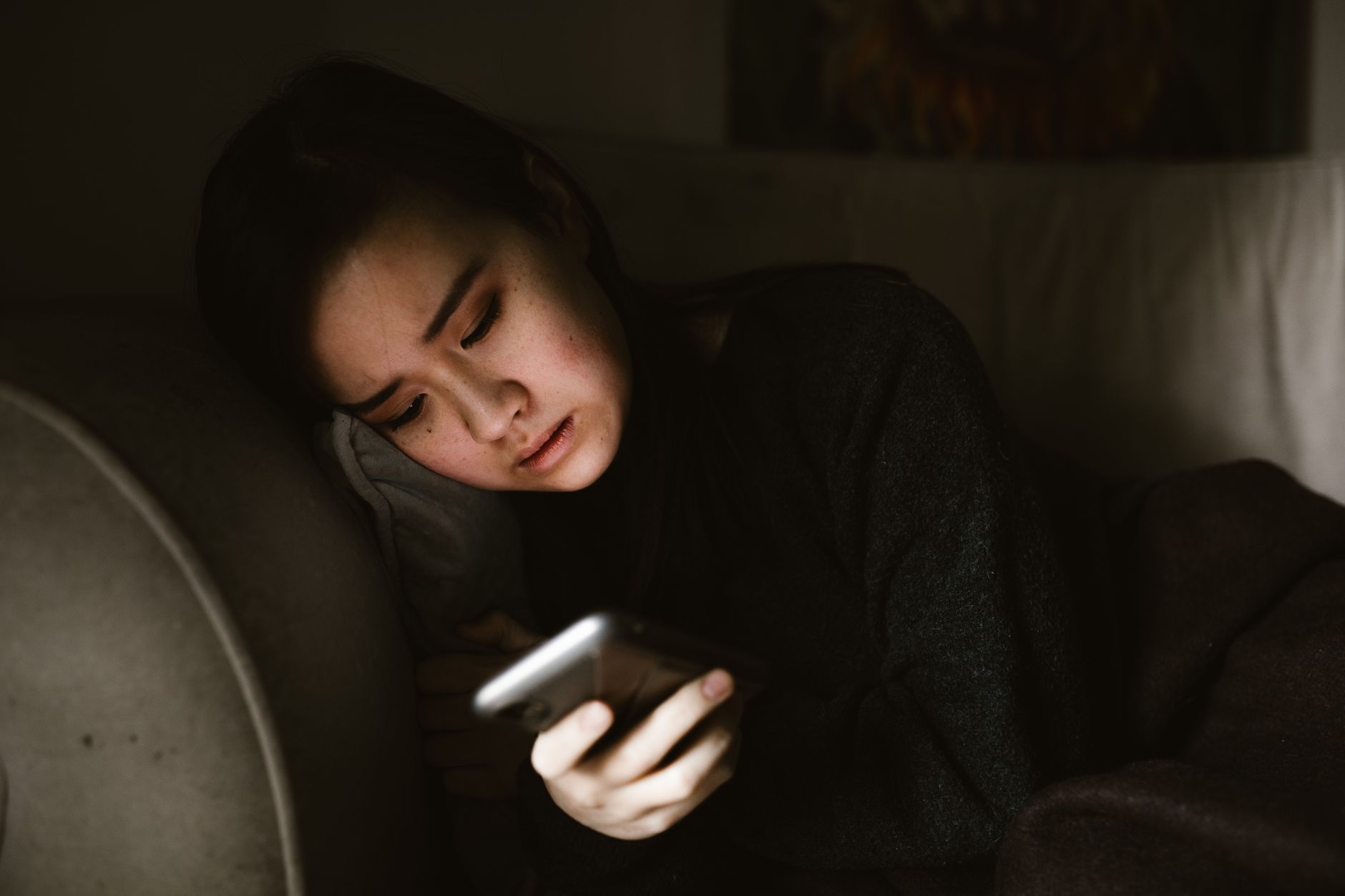 A parent with tired eyes looking at their phone in a dimly lit room, perhaps checking a baby's sleep schedule or seeking information, conveying the exhaustion of new parenthood.