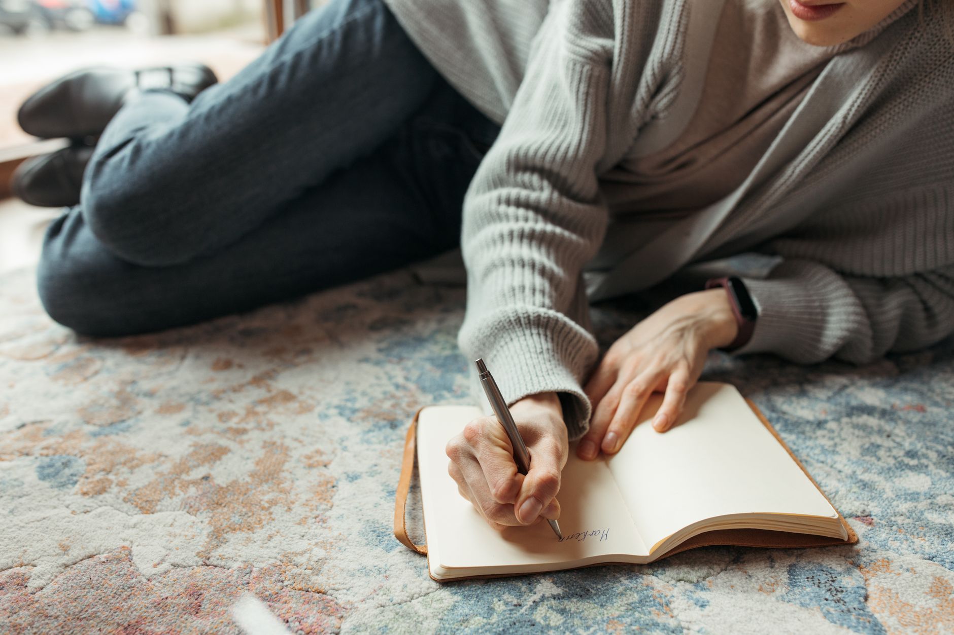A woman sitting on a bed with a laptop, surrounded by pregnancy books and a journal, looking thoughtful