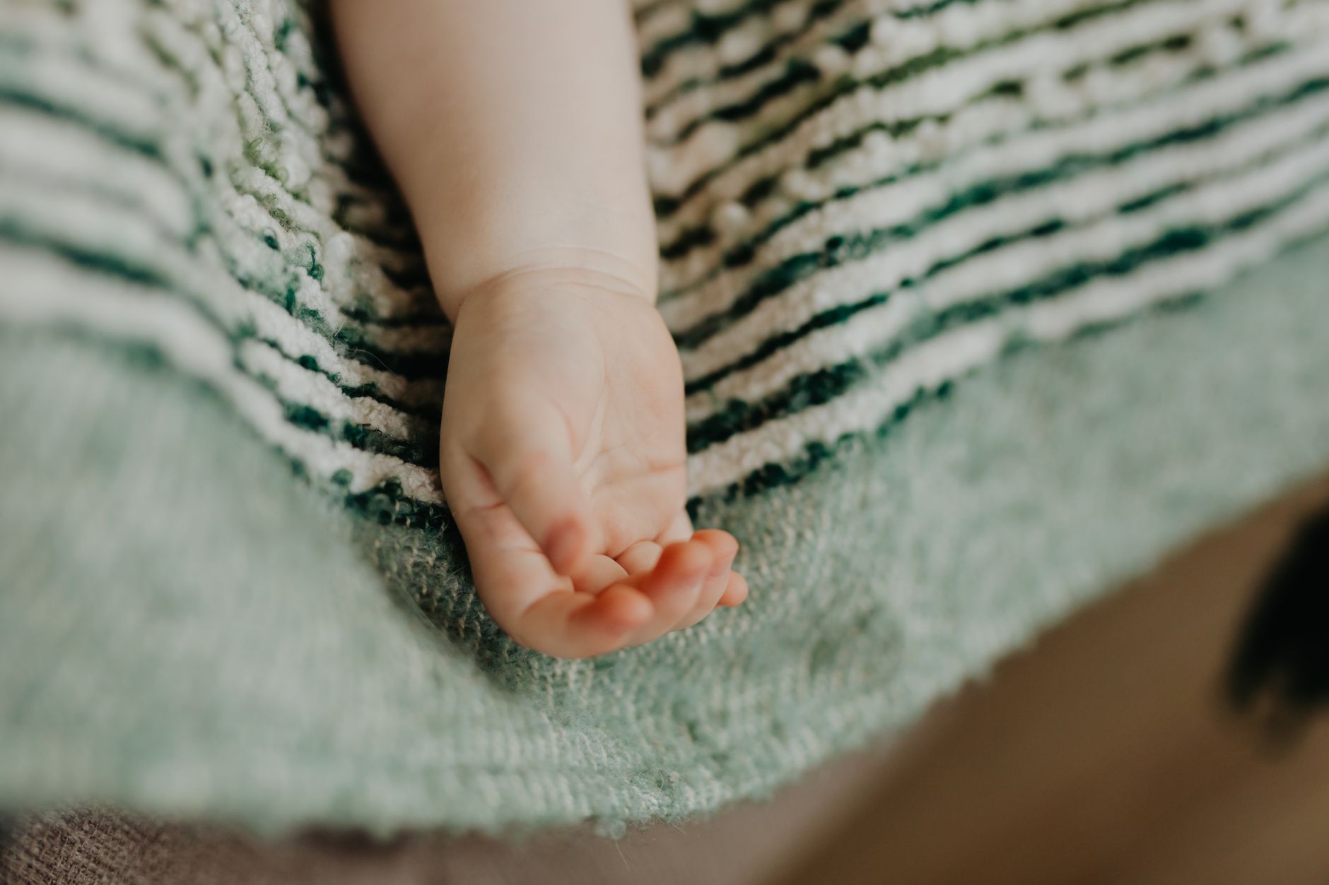 Close‑up of a newborn’s hand with a gentle reflex test being performed, soft natural light, wooden nursery backdrop