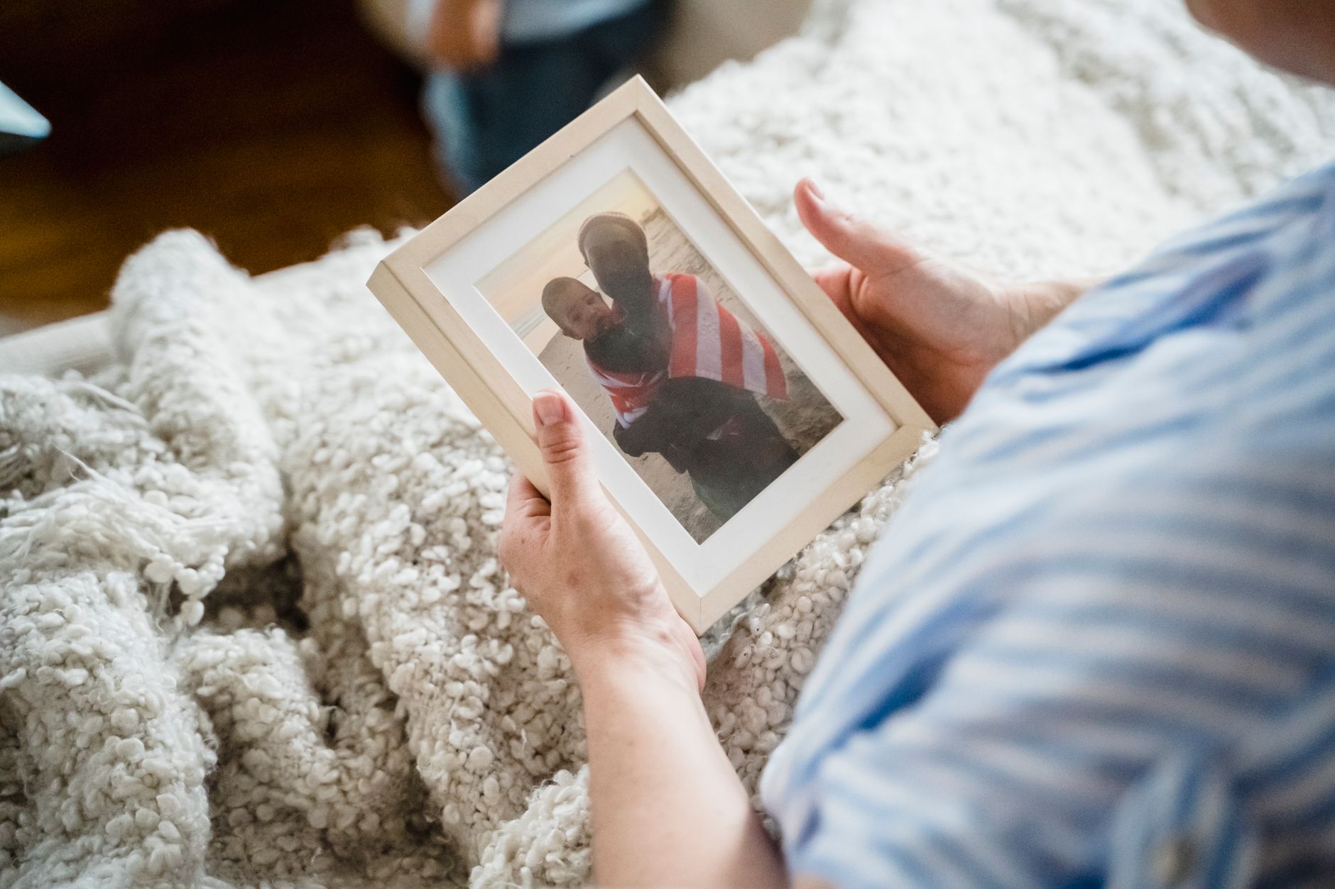 A parent sitting on a couch, holding a framed photo of their baby who passed away in the NICU, during a quiet holiday evening.