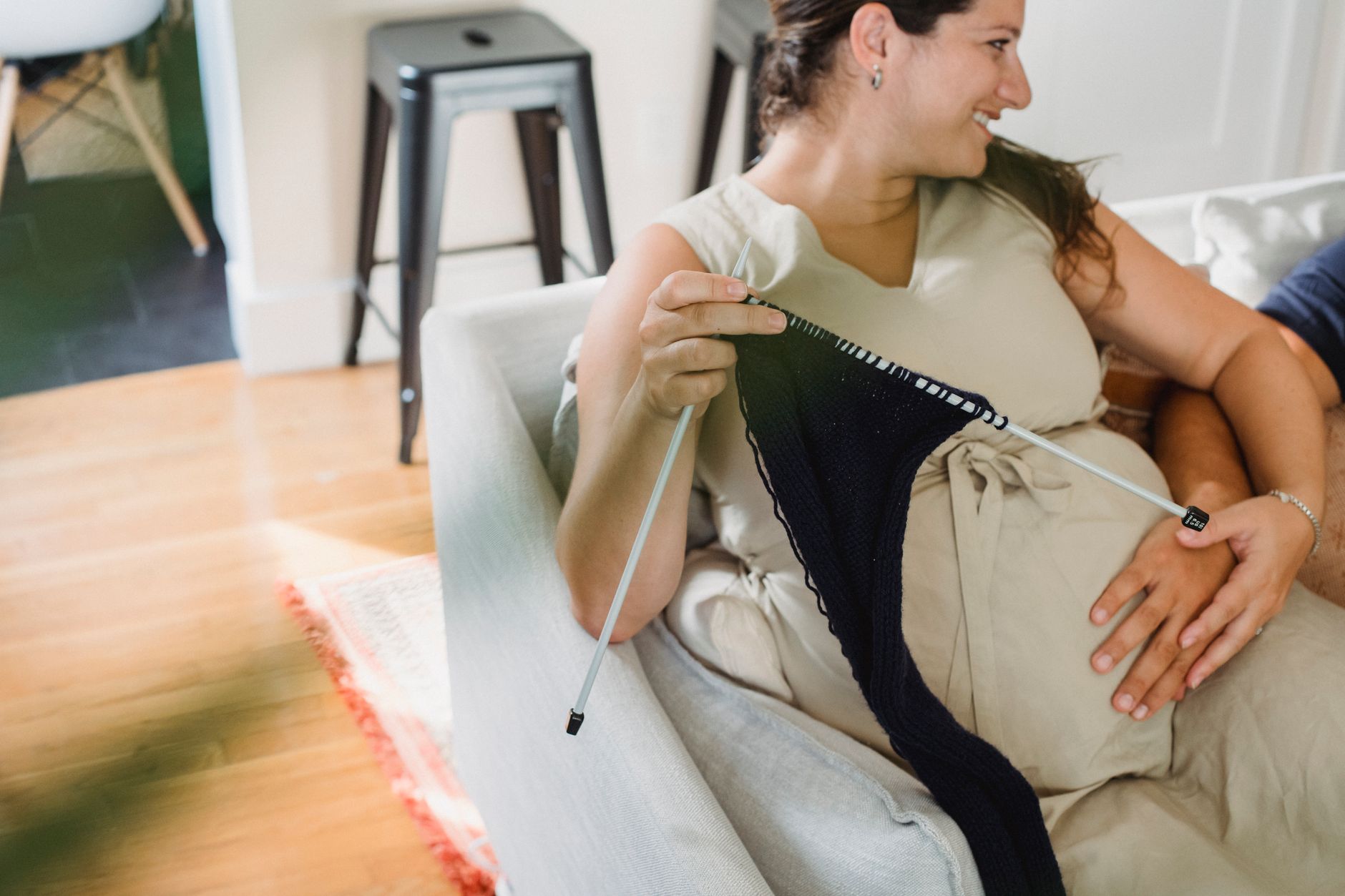 Pregnant woman sitting with a partner on a cozy couch, holding a cup of tea while a fetal monitor rests on her belly, warm natural light