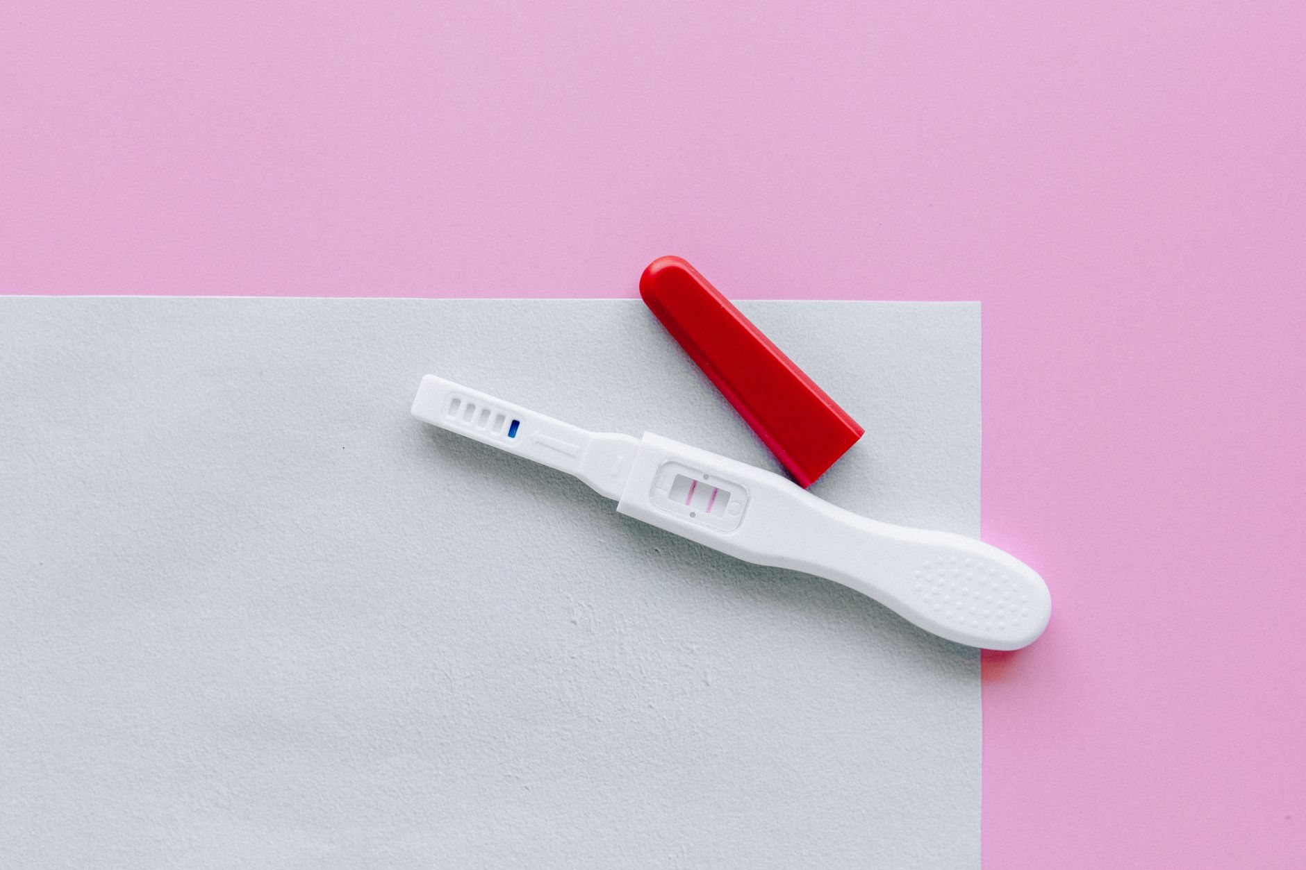 A hand holding a cup of water beside a pregnancy test with a faint pink line, soft natural light on a wooden countertop