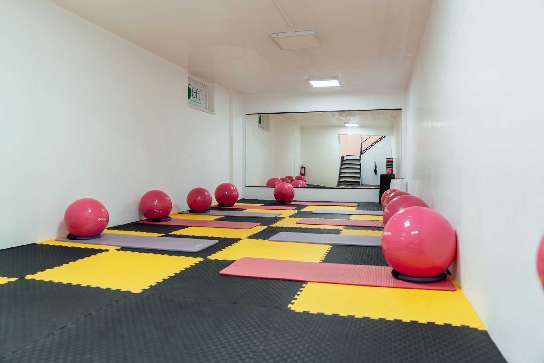 A set of colorful Pilates balls arranged on a wooden floor beside a yoga mat, bright natural light highlighting the equipment