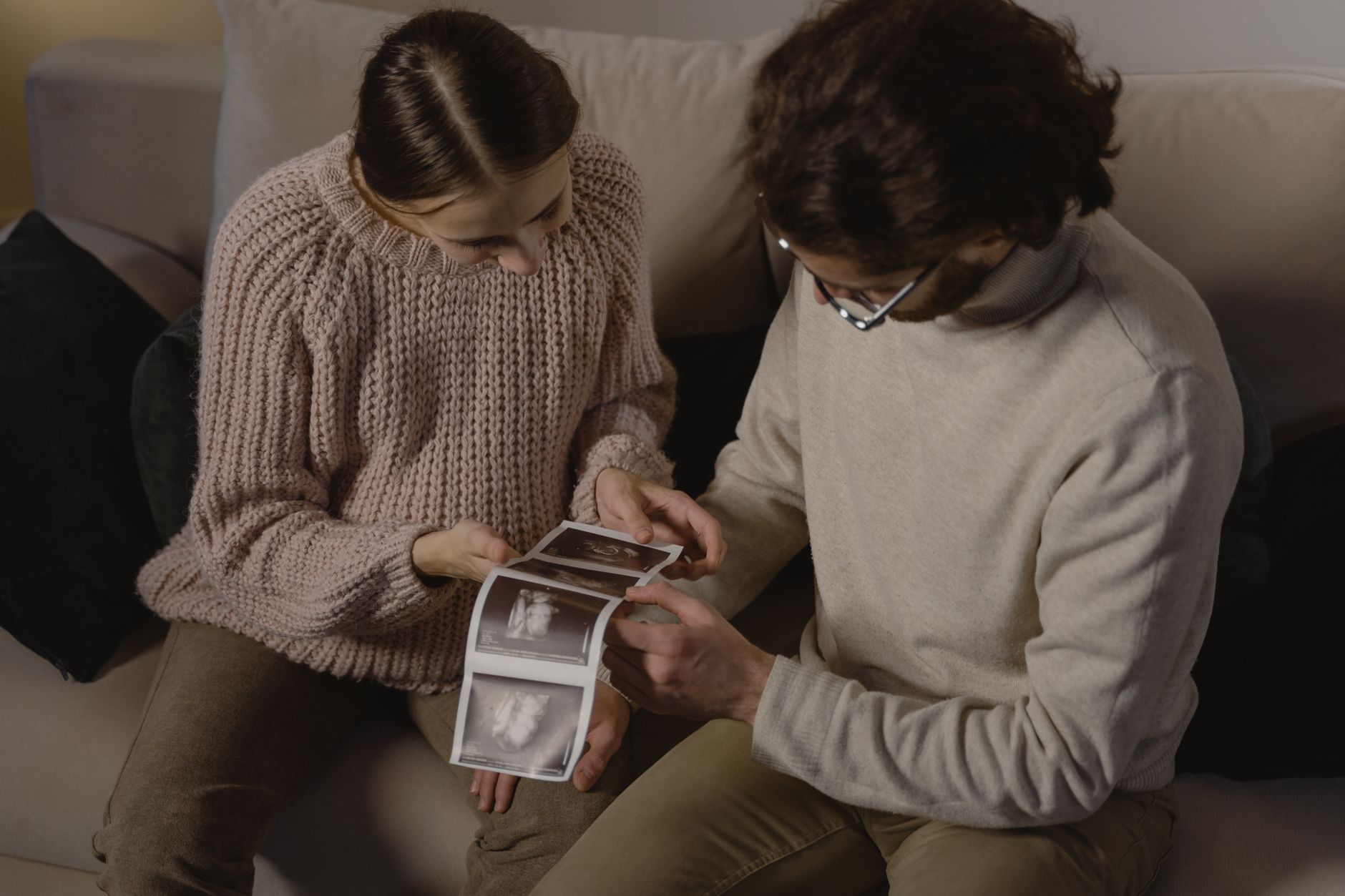 Pregnant woman sitting on a couch with a tablet, reviewing ultrasound images of her baby's blood flow, soft natural lighting, cozy home setting