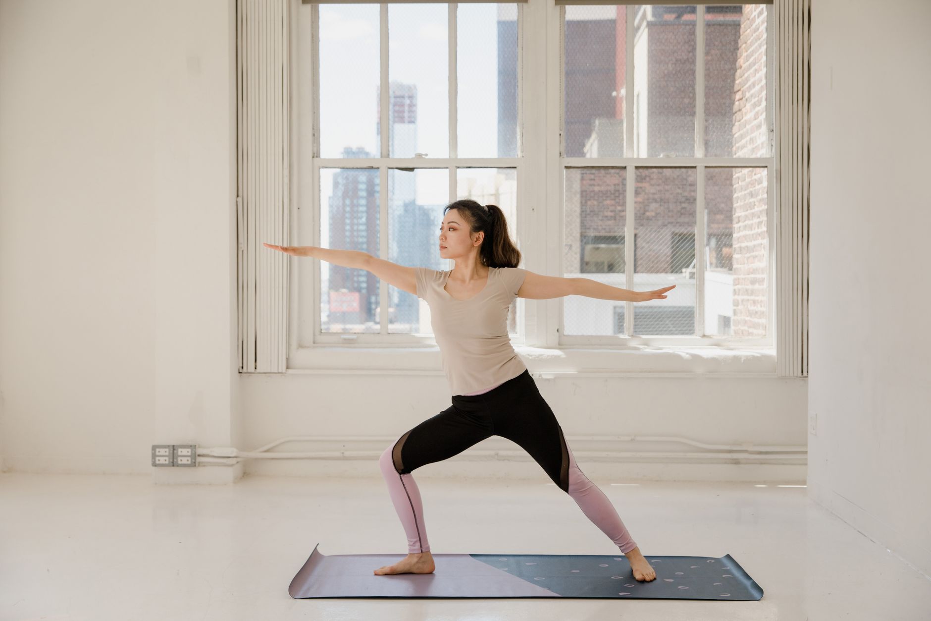 Woman in comfortable clothing gently stretching in a sunlit room, focusing on mindful movement and self-care for her postpartum body.