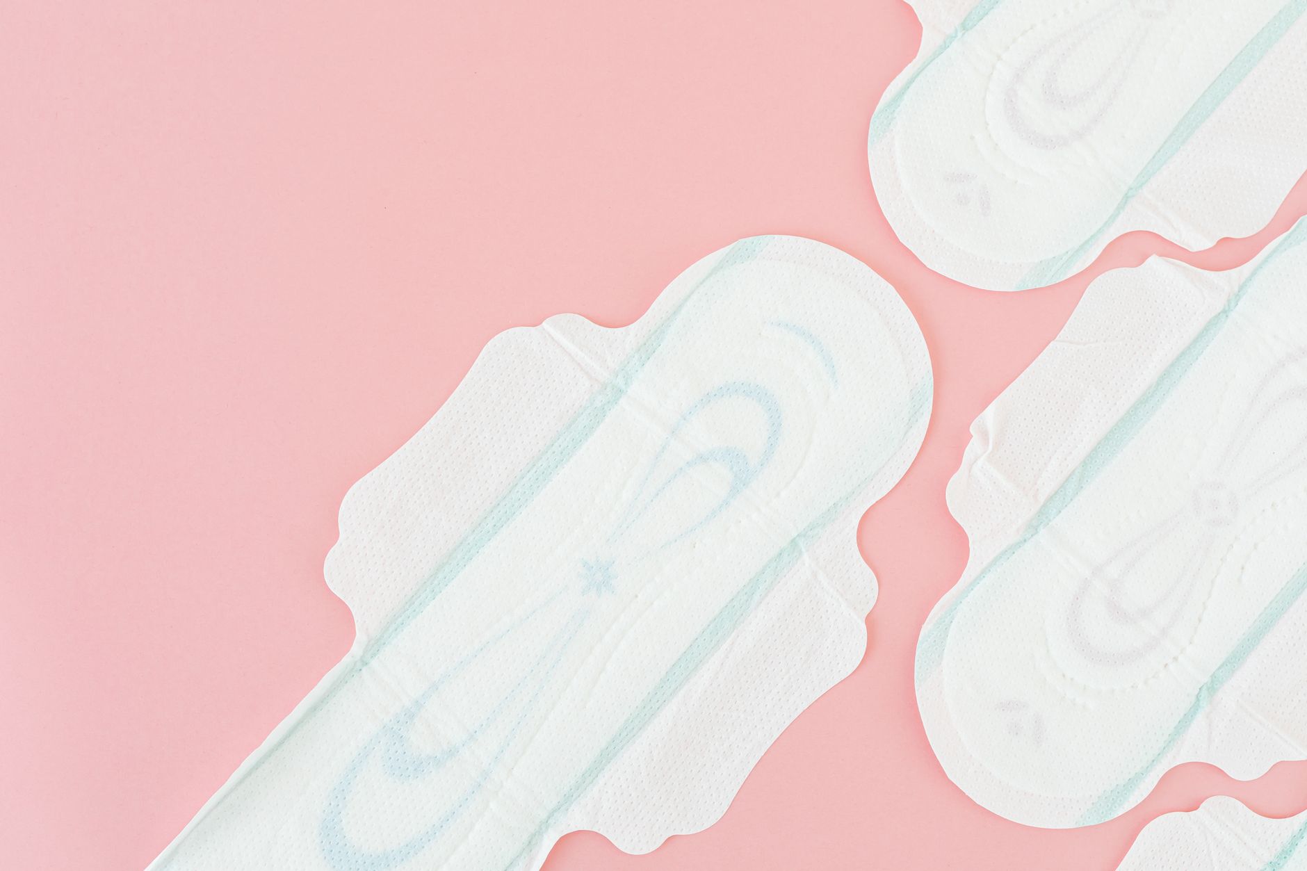 Close‑up of a stack of soft, breathable postpartum incontinence pads beside a newborn blanket on a light wooden surface