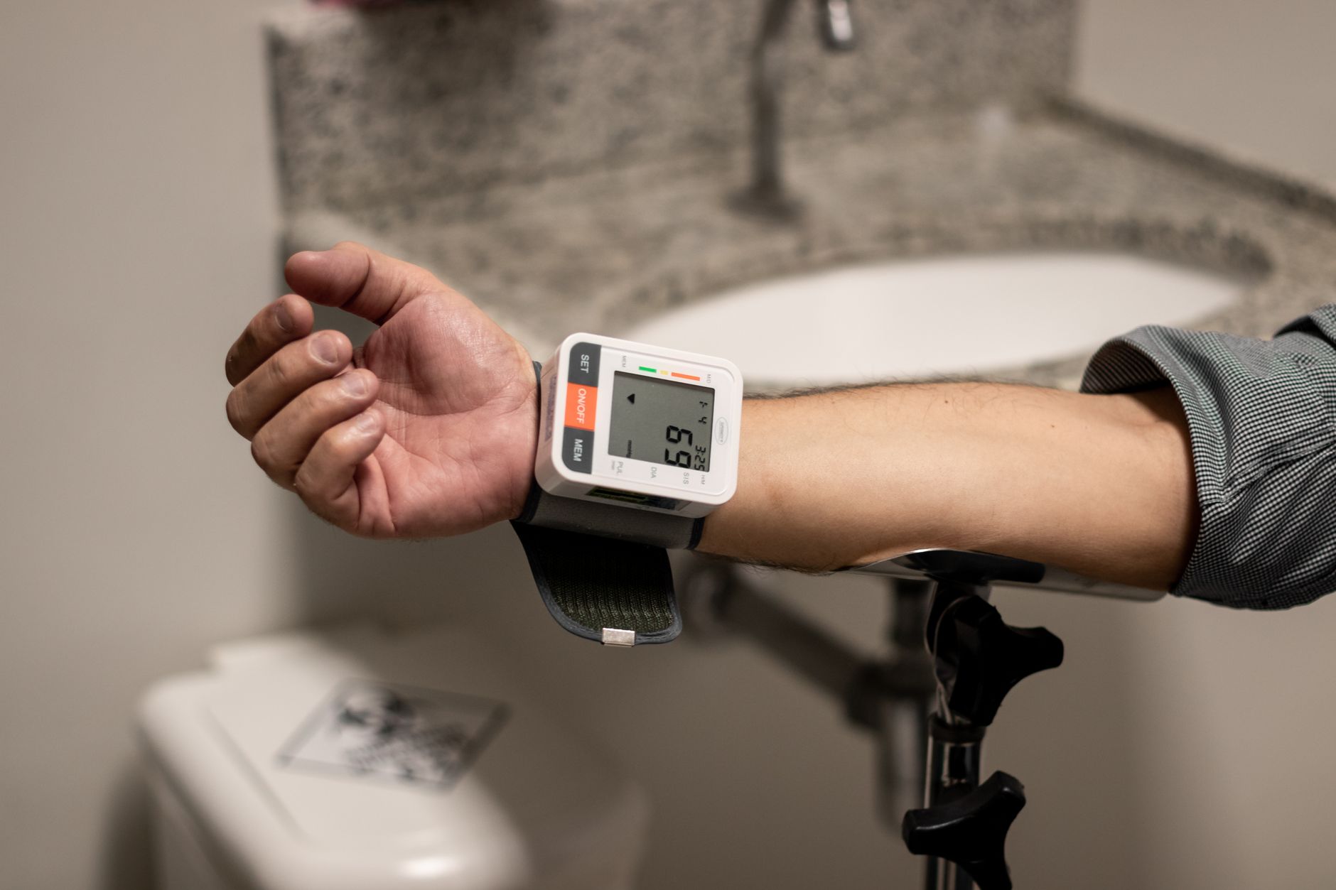 A woman's arm with a blood pressure cuff, showing an at-home blood pressure monitor displaying a reading, in a clean, bright home setting
