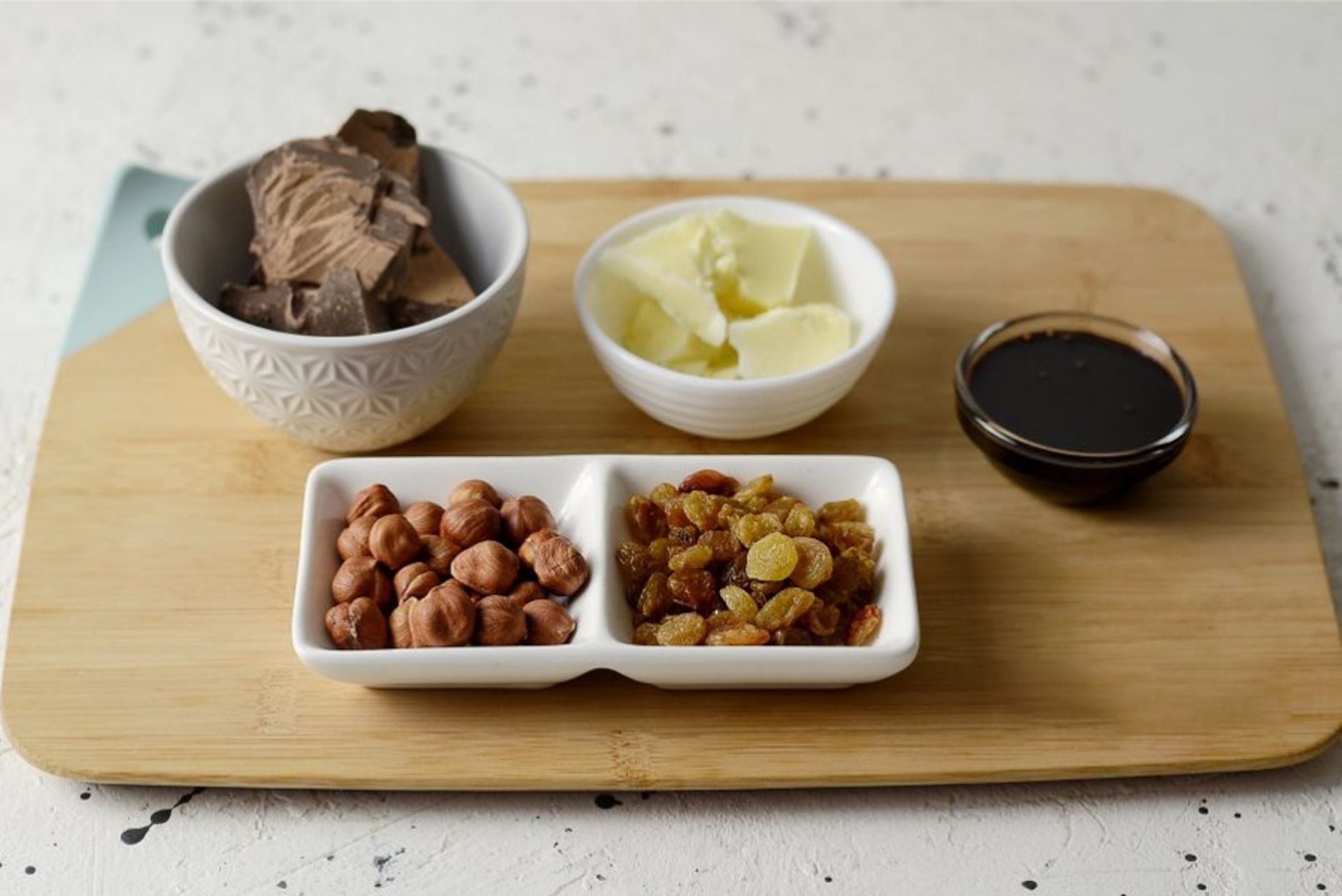 Close‑up of a hand holding a small bowl of mixed nuts, dried fruit, and dark chocolate chips on a rustic wooden surface, soft natural lighting