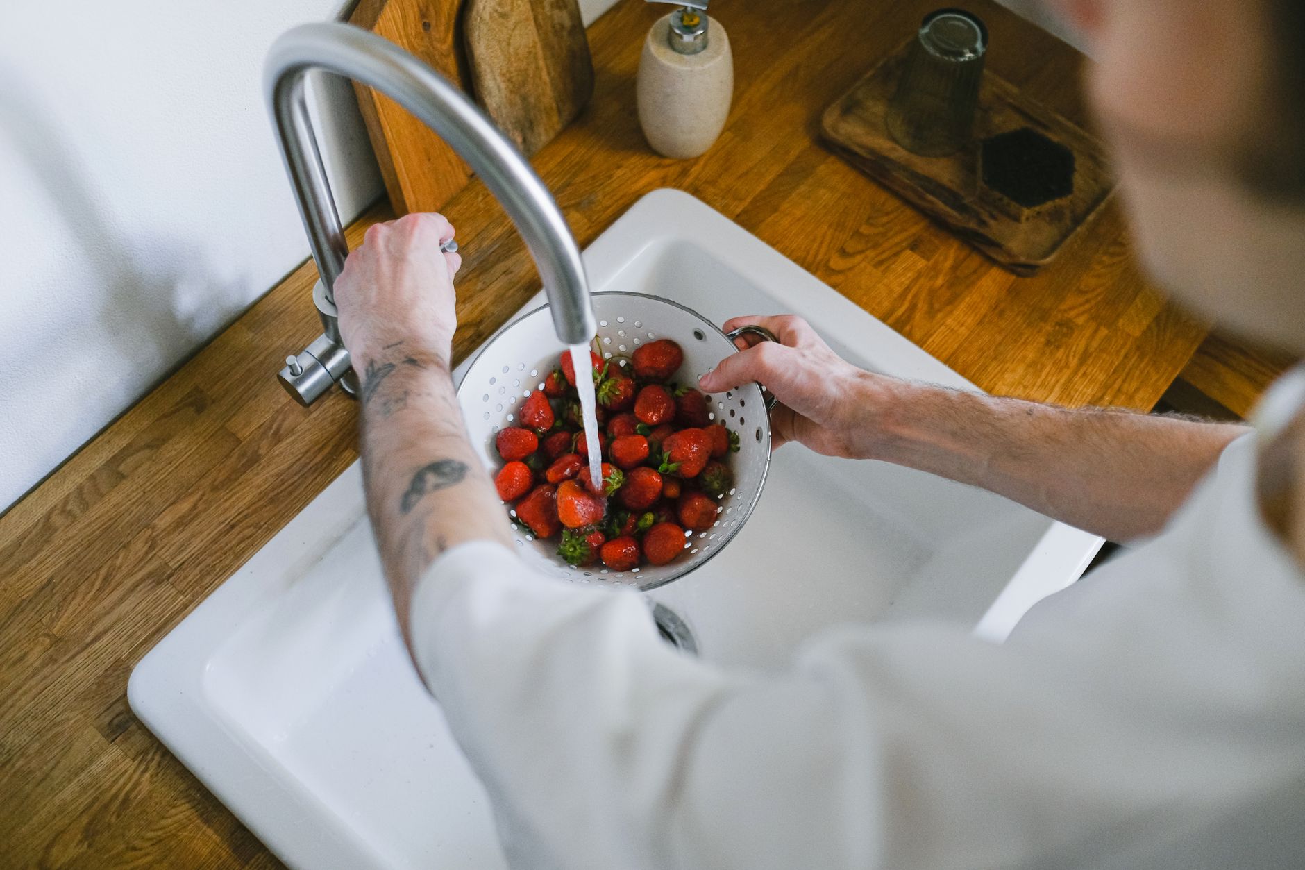 A person gently washing fresh berries under running water in a kitchen sink, emphasizing food hygiene