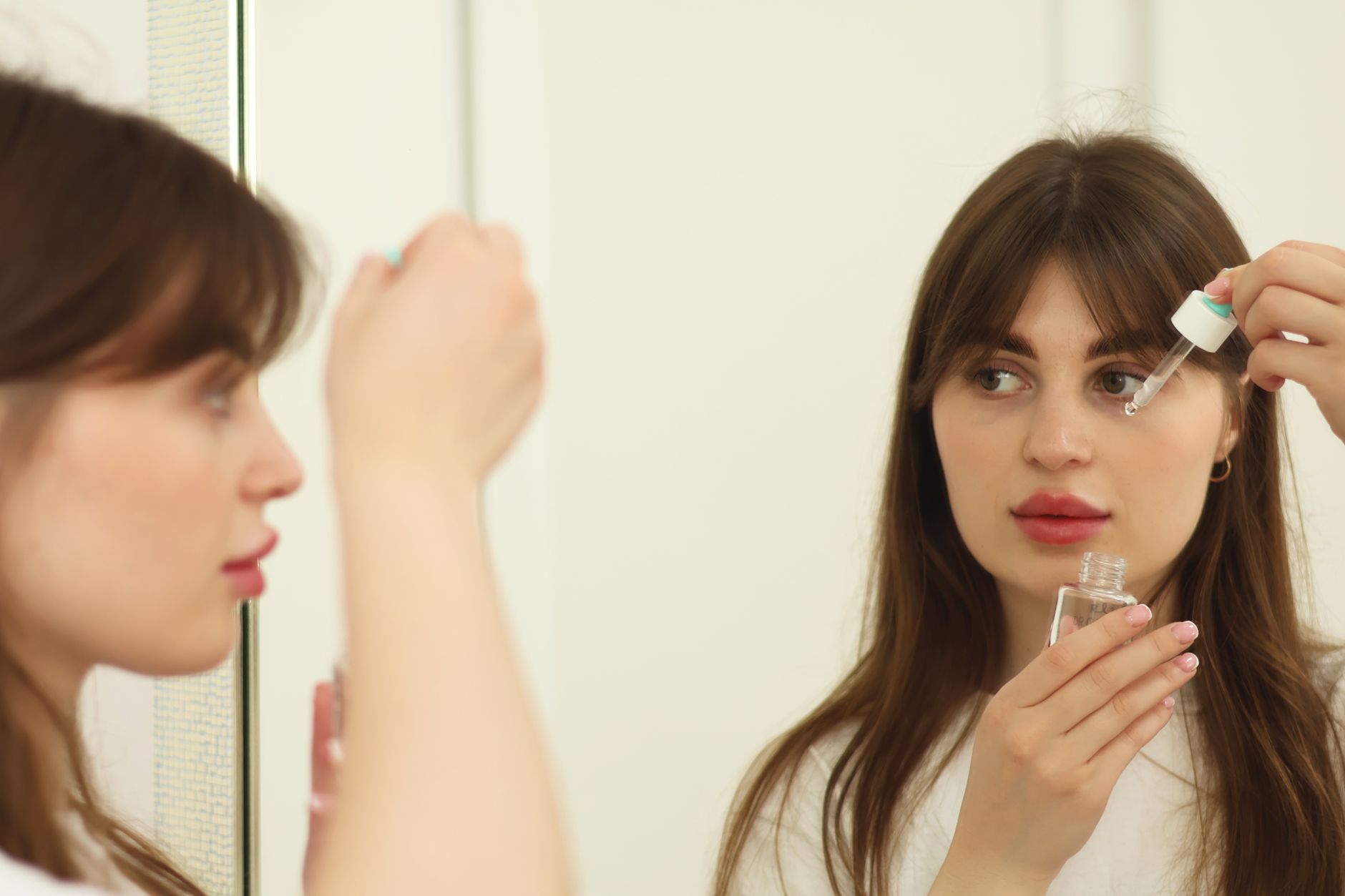 A woman gently applying a pregnancy-safe facial serum, with a clean and bright bathroom background, suggesting a self-care routine.
